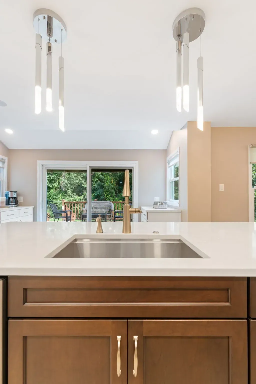 Modern kitchen with white island, wood cabinets, and pendant lights facing a patio view In Bucks County PA