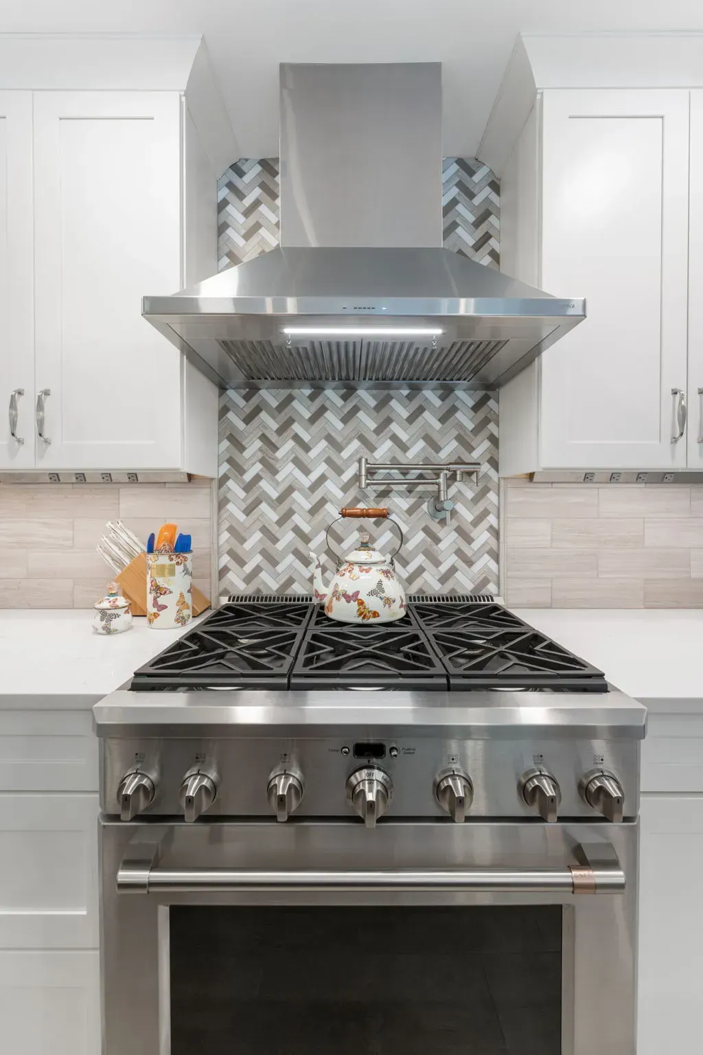 Modern kitchen with stainless steel stove, range hood, and white cabinets with patterned backsplash In Bucks County PA