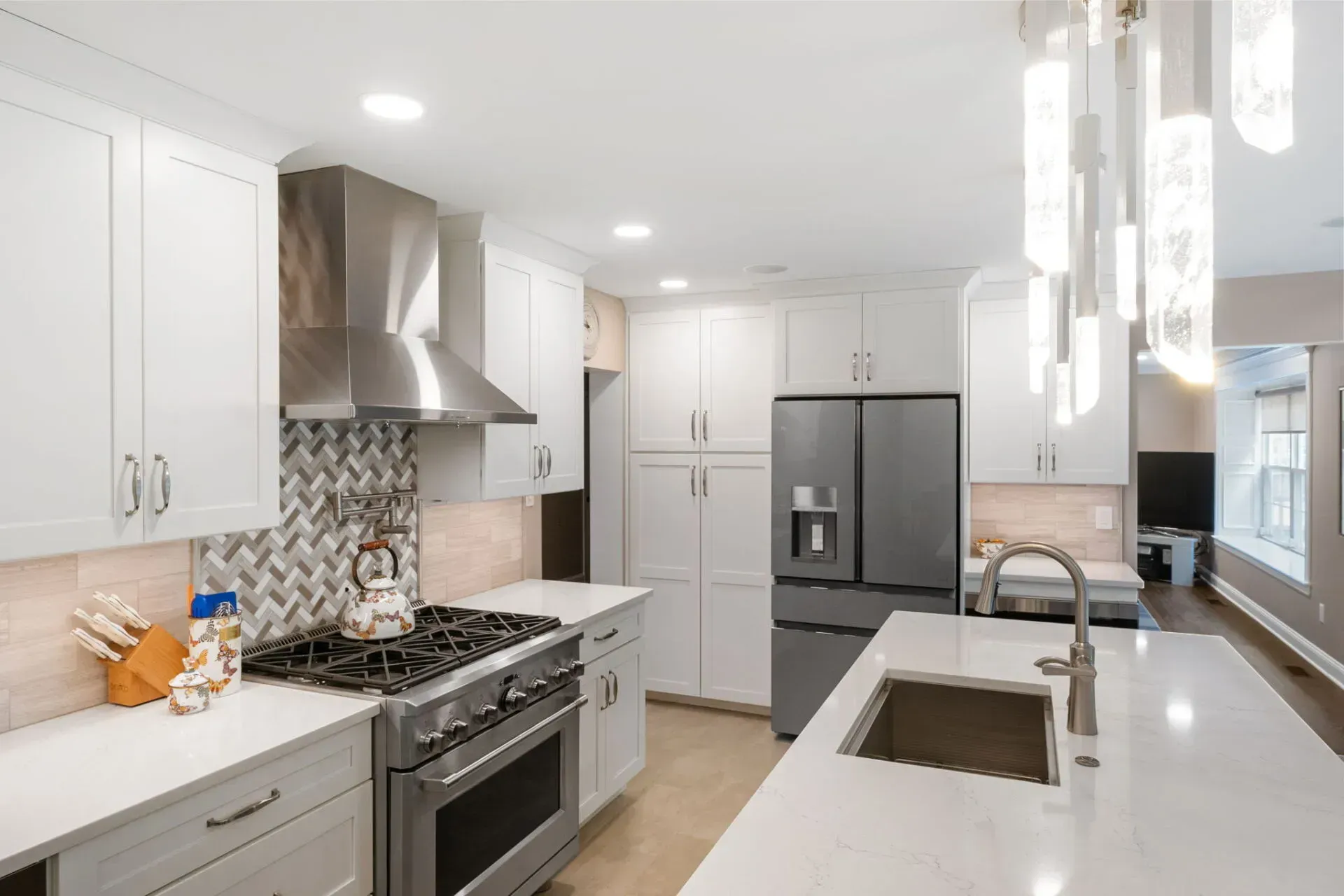 Bright modern kitchen with white cabinets, stainless appliances, island sink, and pendant lights In Bucks County PA