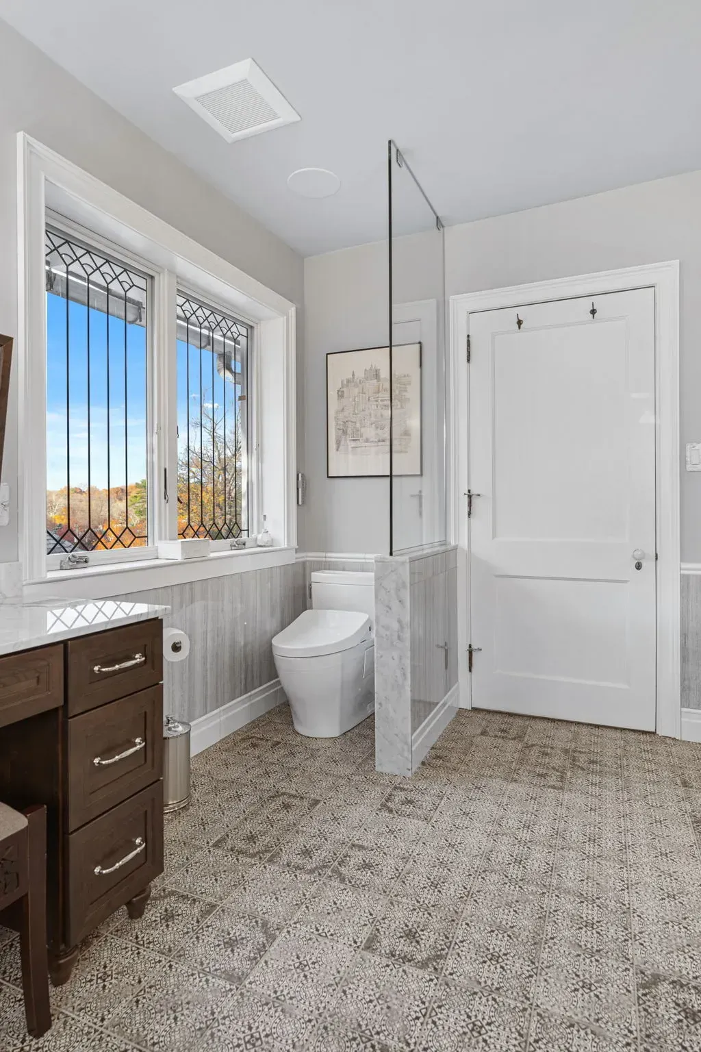 Bright modern bathroom with white walls, dark wood vanity, window, toilet, and glass shower partition in Bucks County PA