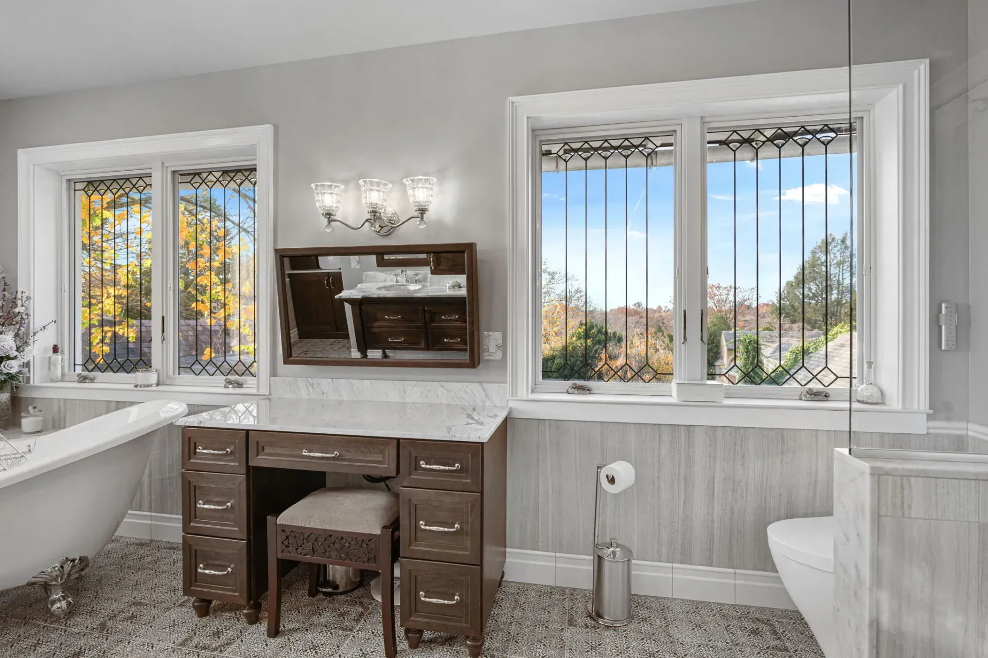 Bright bathroom with double windows, vanity desk, wall mirror, and white toilet in Bucks County PA