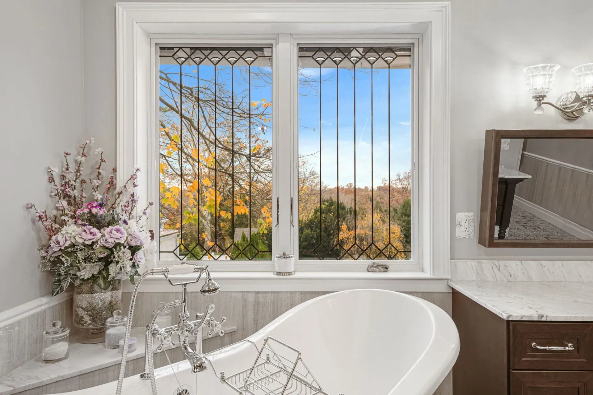 Bright bathroom with a white bathtub, vanity mirror, and window overlooking autumn trees in Bucks County
