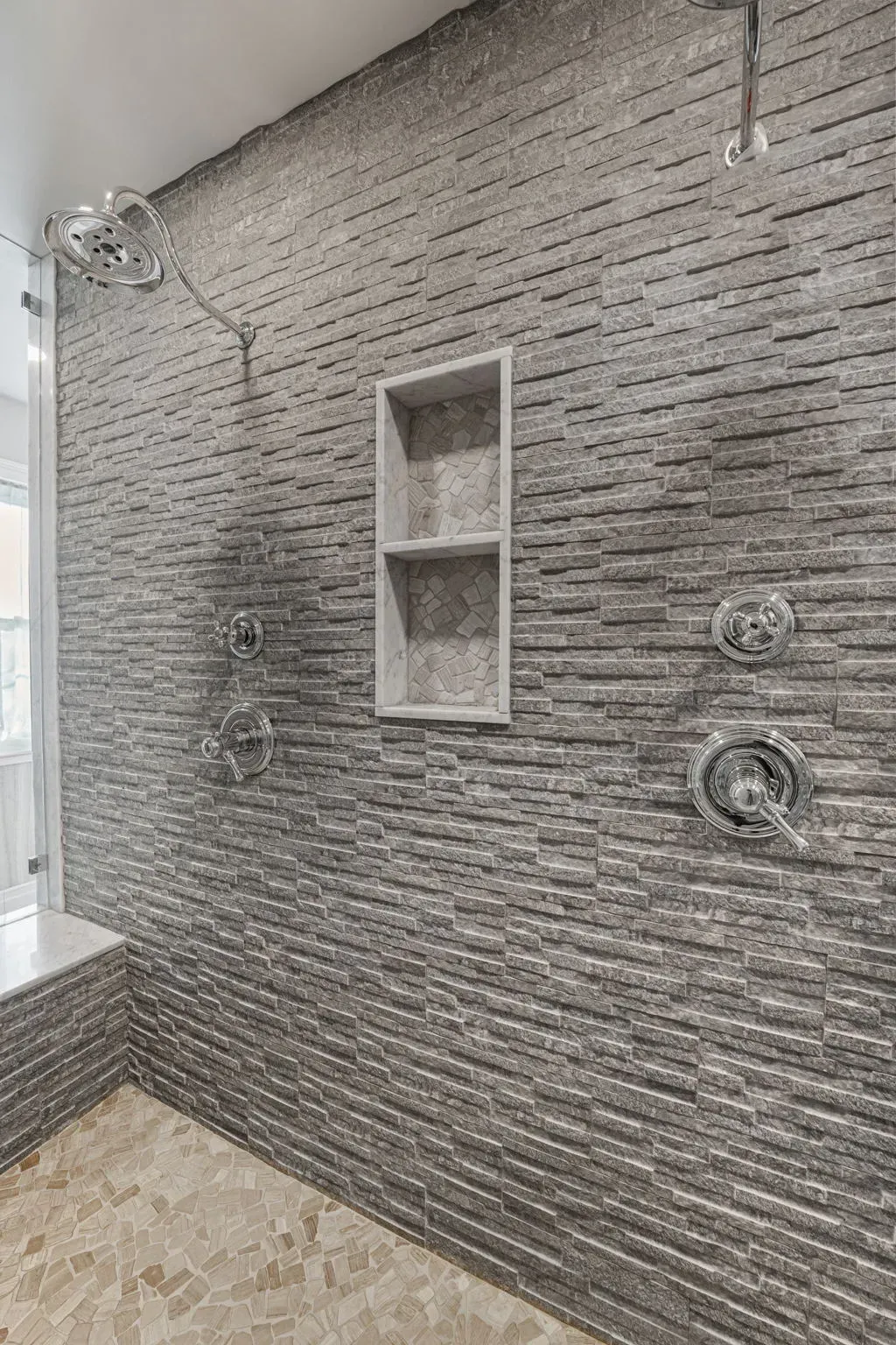 Stone-tiled shower wall with built-in niche and multiple chrome shower fixtures in Bucks County PA