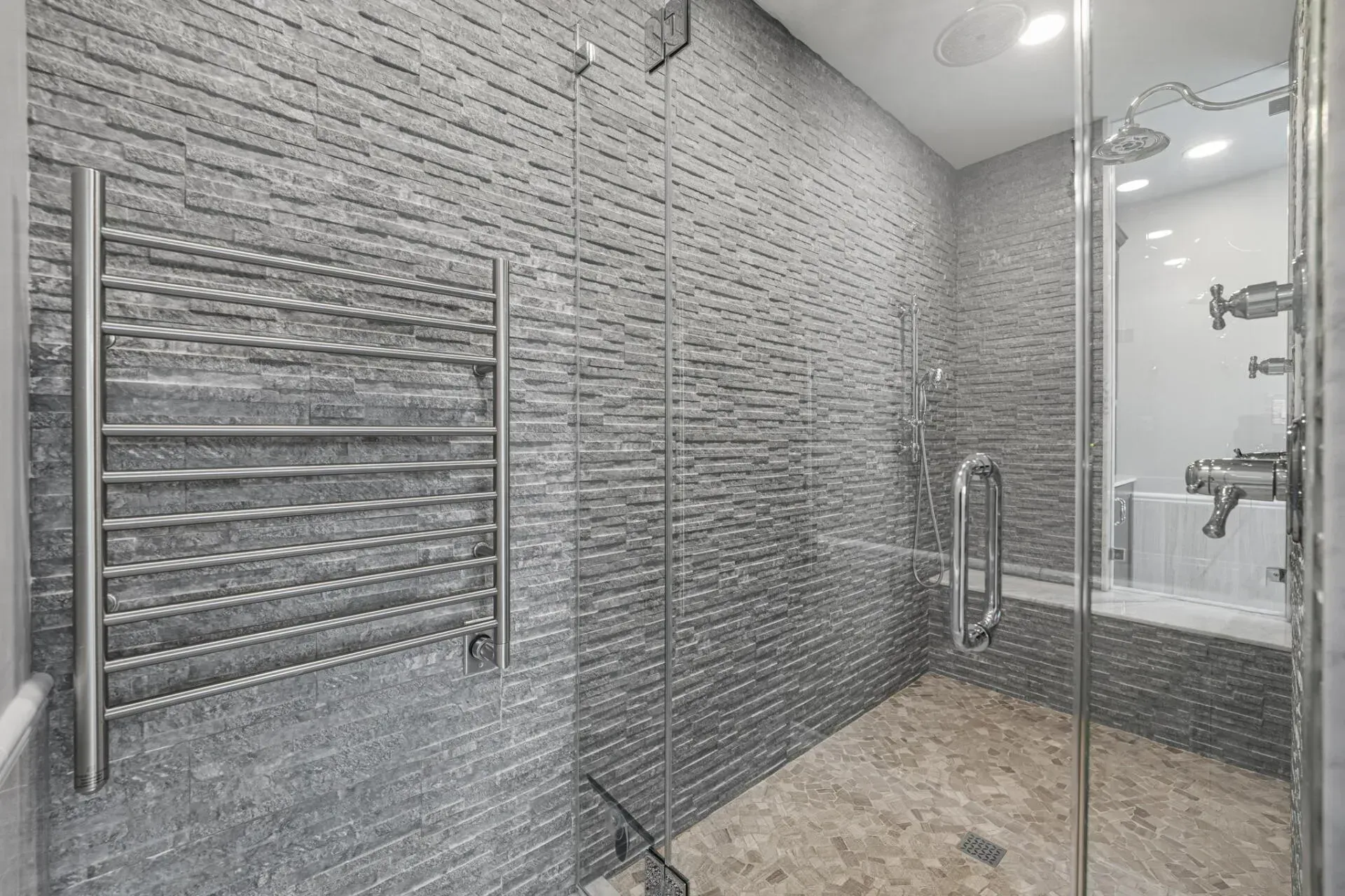 Modern tiled walk-in shower with glass door and chrome towel warmer, viewed from the entrance In Bucks Country PA