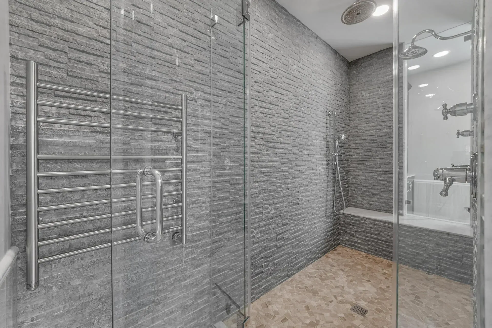 Modern gray tiled walk-in shower with glass door, chrome fixtures, and pebble floor In Bucks Country PA