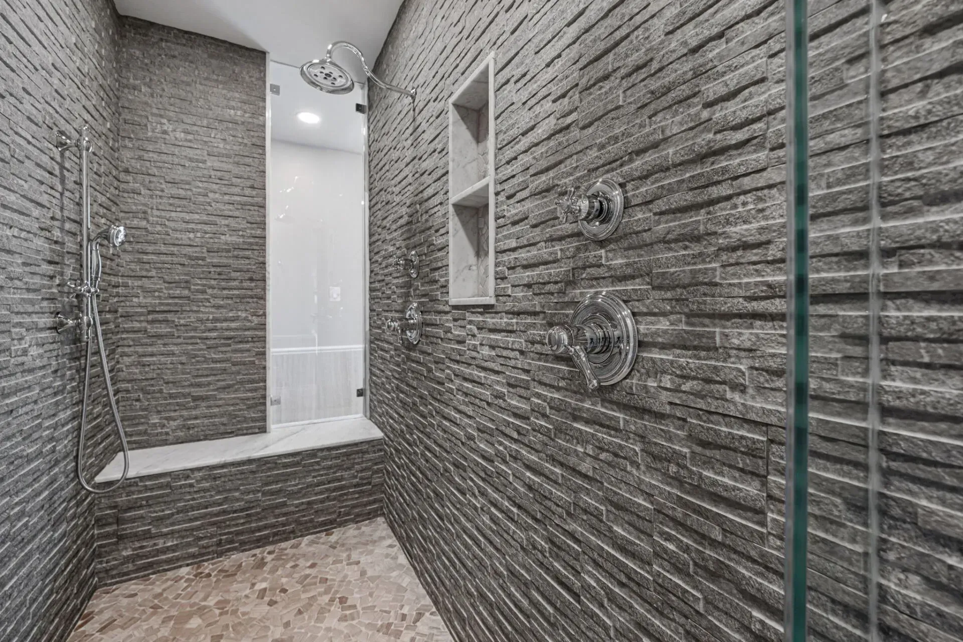 Modern gray-tiled walk-in shower with glass enclosure, rainfall showerhead, bench, and mosaic stone floor In Bucks Country PA