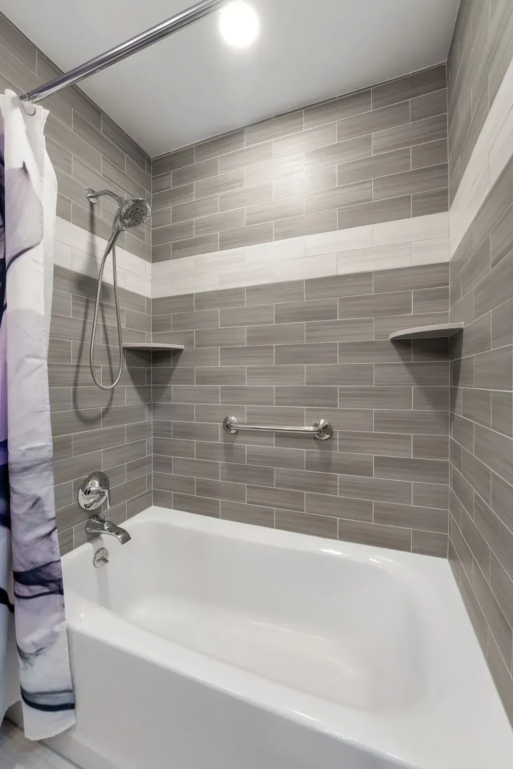 Small tiled bathroom with a white bathtub, gray shower walls, and a handheld showerhead In Bucks County PA