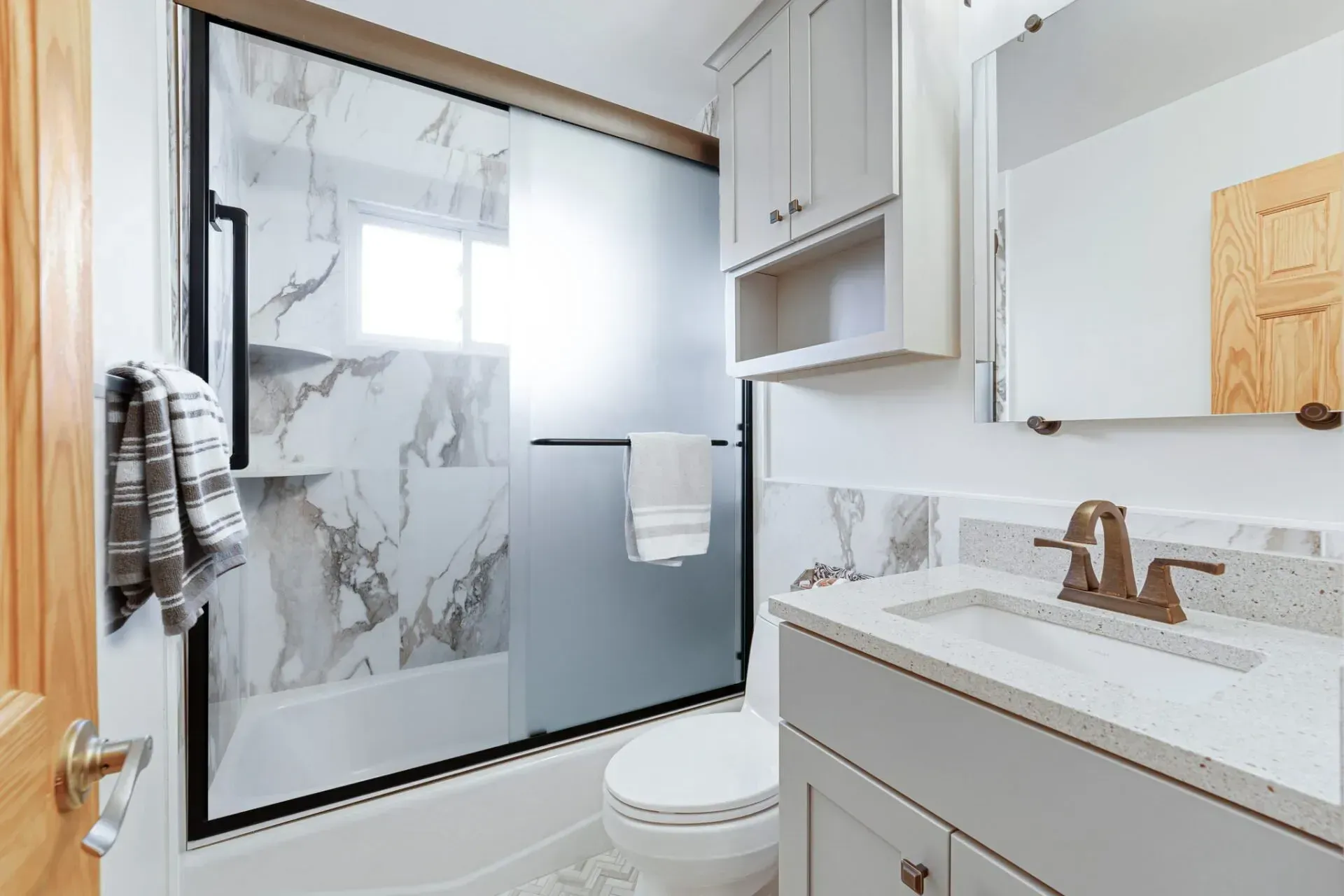 Modern bathroom with glass shower, white vanity, and frosted window beside a toilet In Bucks County PA