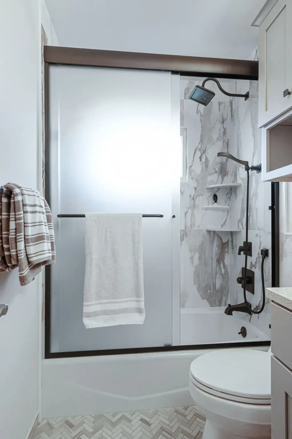 Small bathroom with frosted window, shower, towel, and toilet in a modern white interior In Bucks County PA