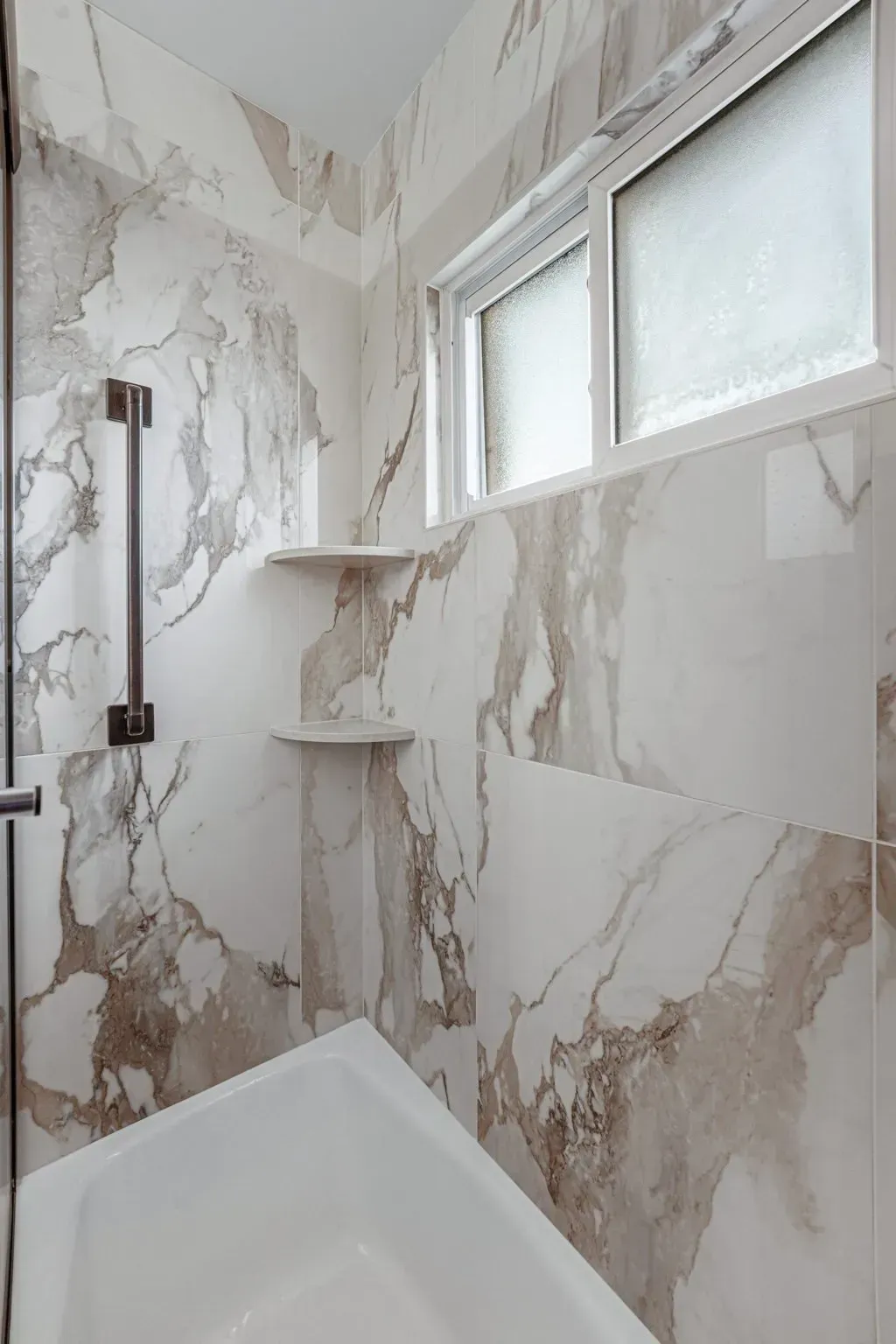Modern shower with marble-pattern tile, built-in corner shelves, and frosted window In Bucks County PA