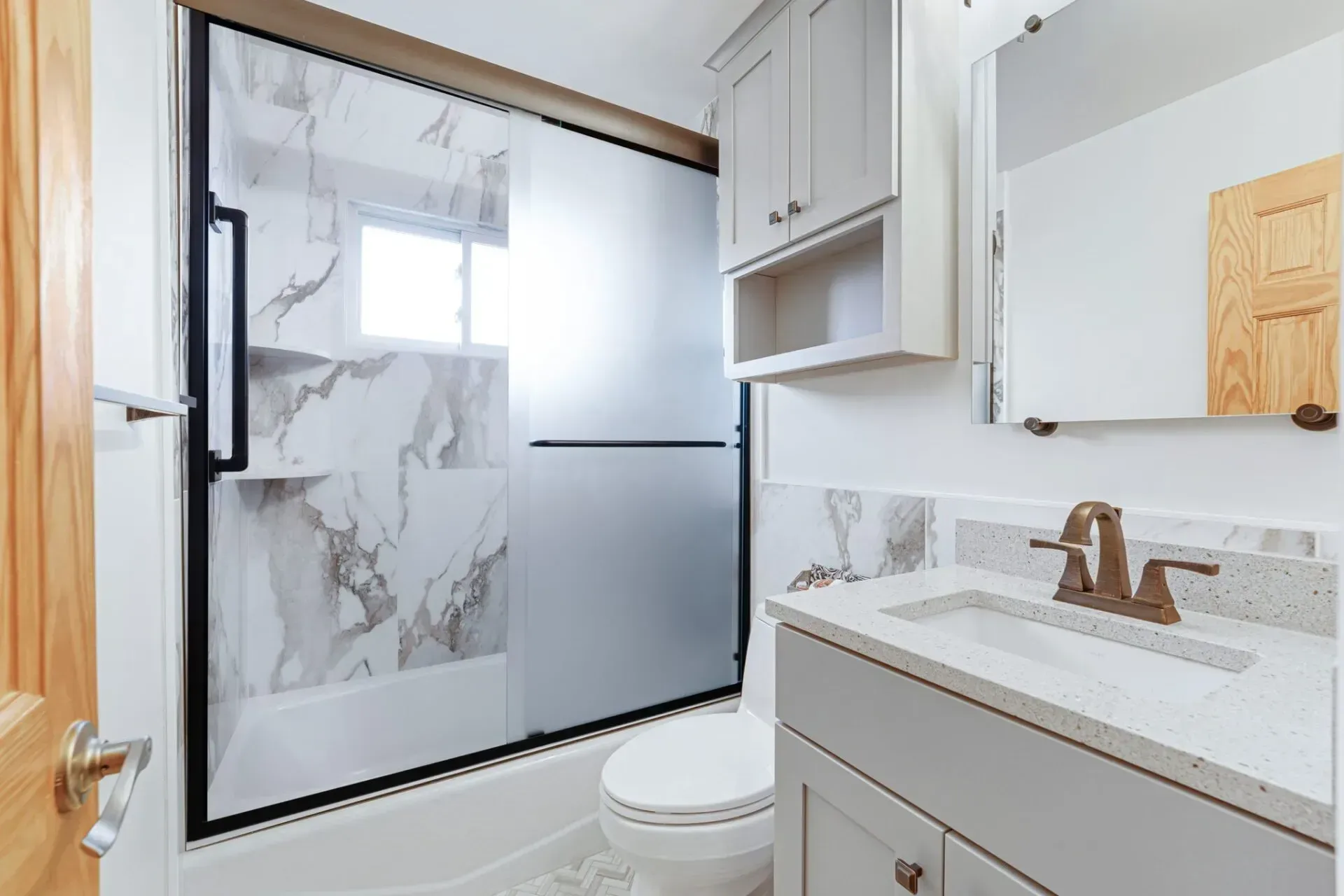 Modern bathroom with marble shower, white vanity, and toilet near a frosted glass door In Bucks County PA