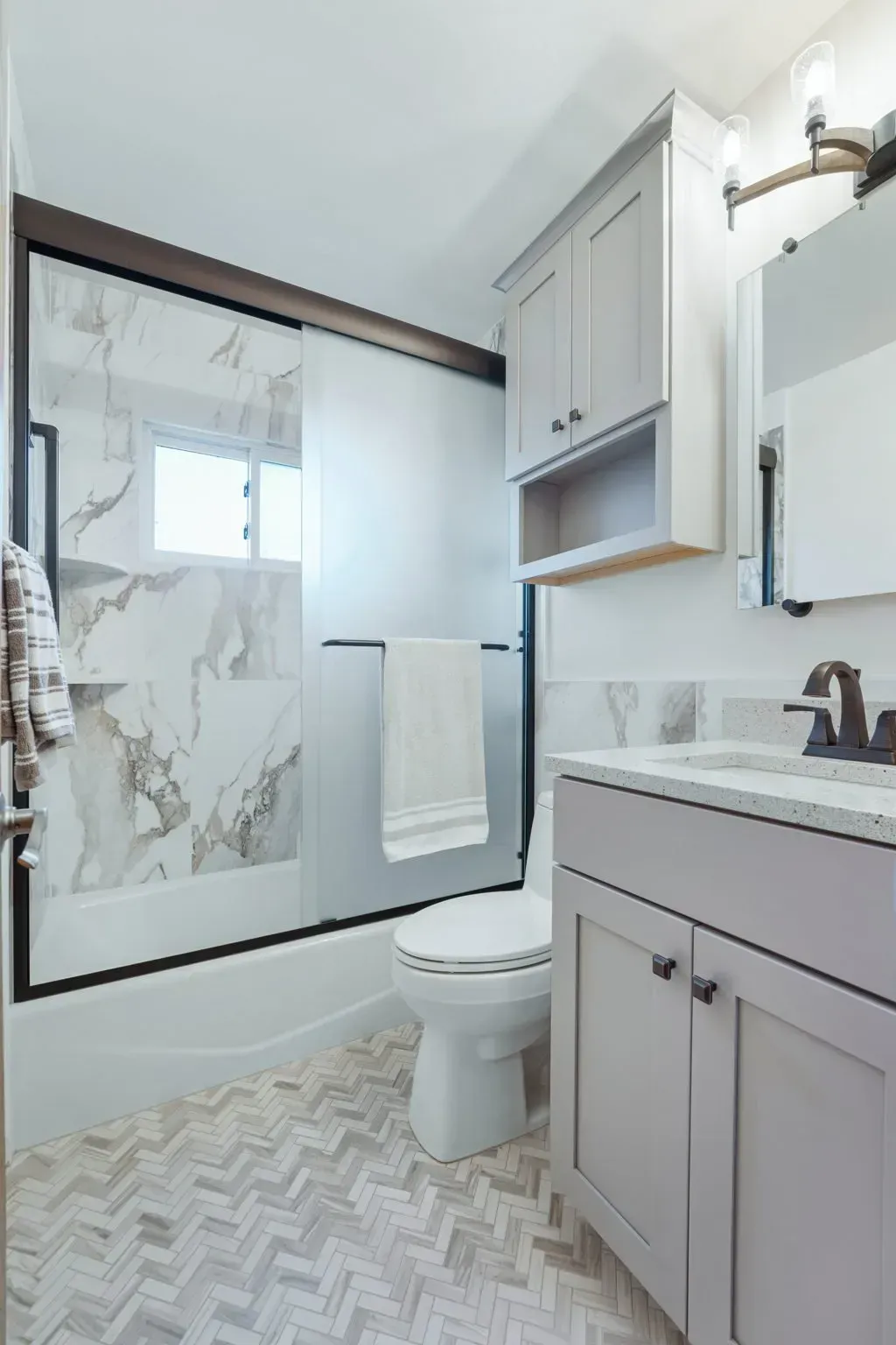 Bright bathroom with gray vanity, toilet, glass shower, and patterned rug in a light, modern space In Bucks County PA
