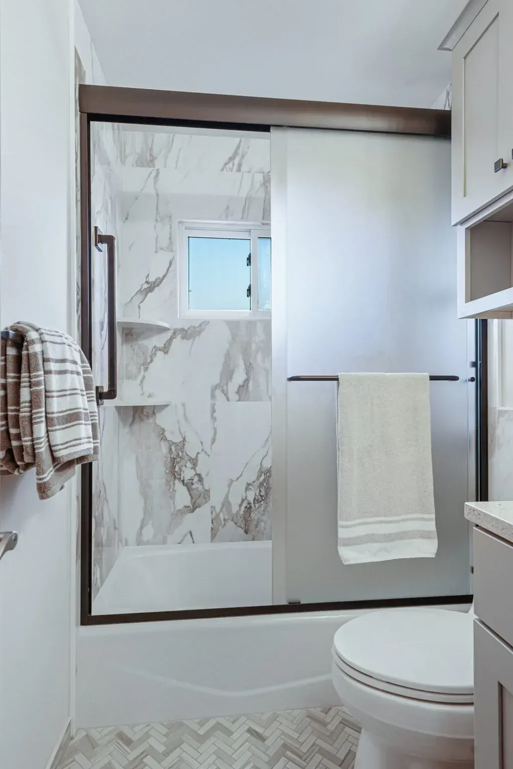 Small bathroom with a glass shower door, marble-look tile, white towel, and toilet visible In Bucks County PA