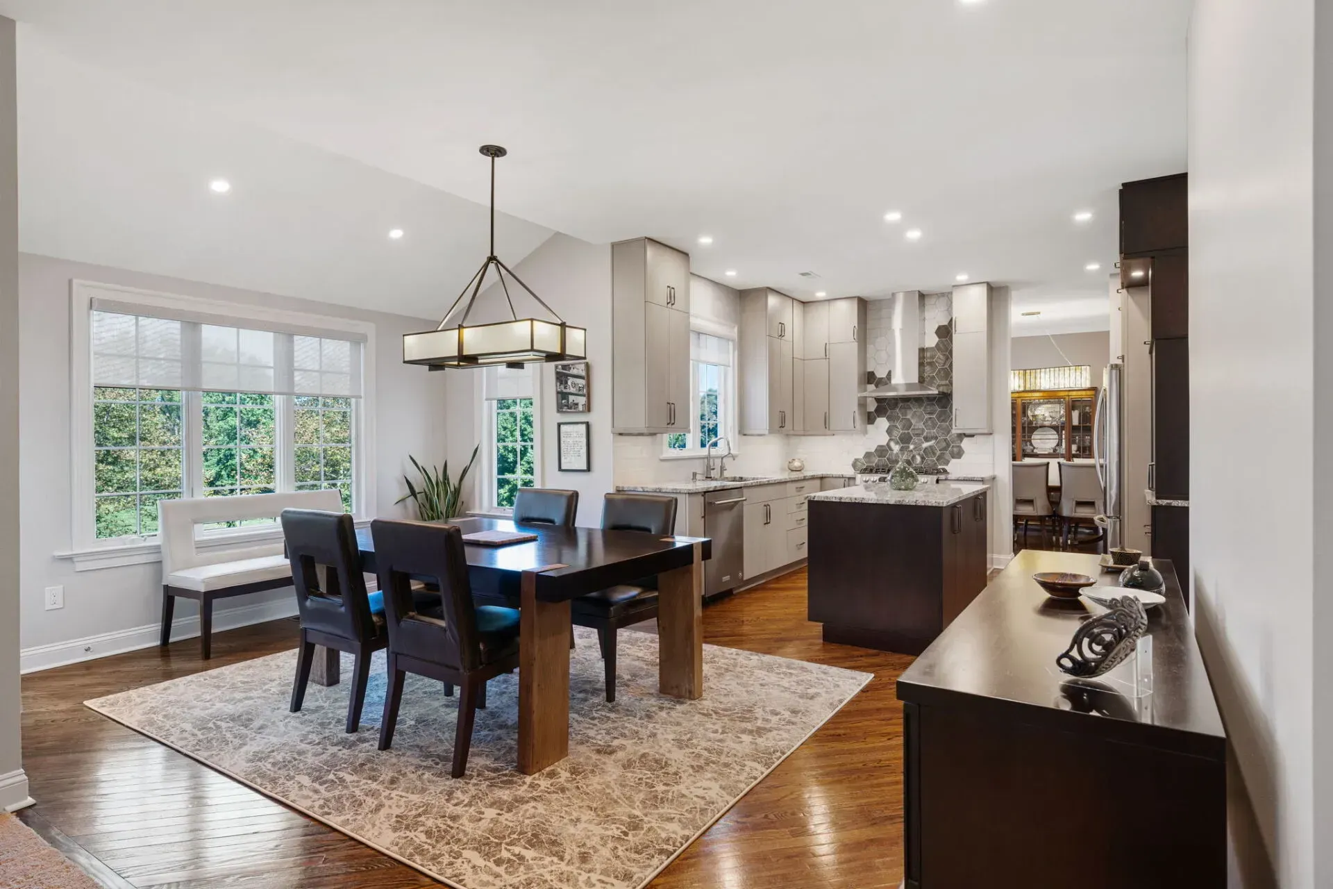 Bright modern kitchen and dining area with dark wood table, island, and large windows In Bucks County PA
