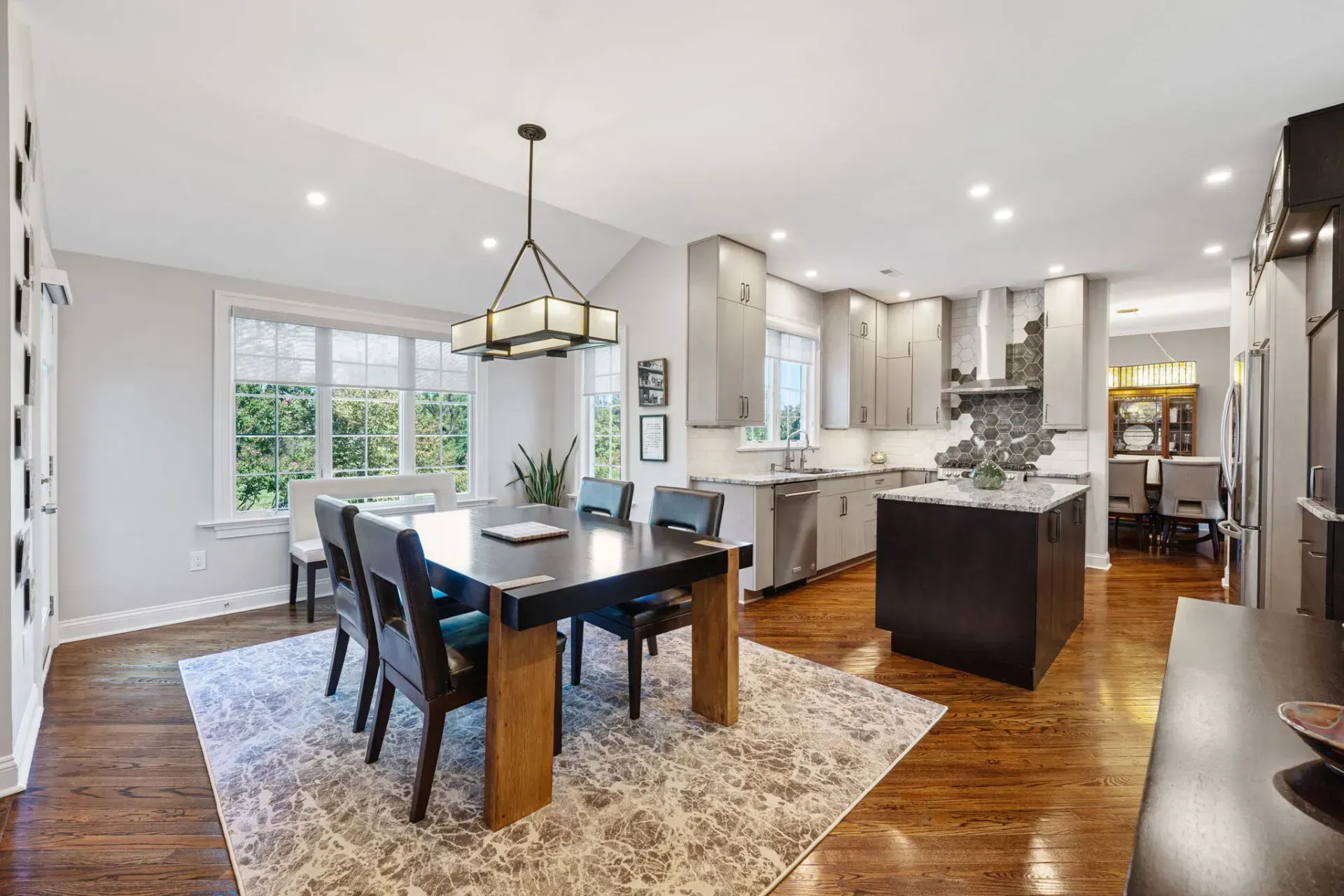 Bright open dining room and kitchen with dark table, island, hardwood floors, and white cabinets In Bucks County PA