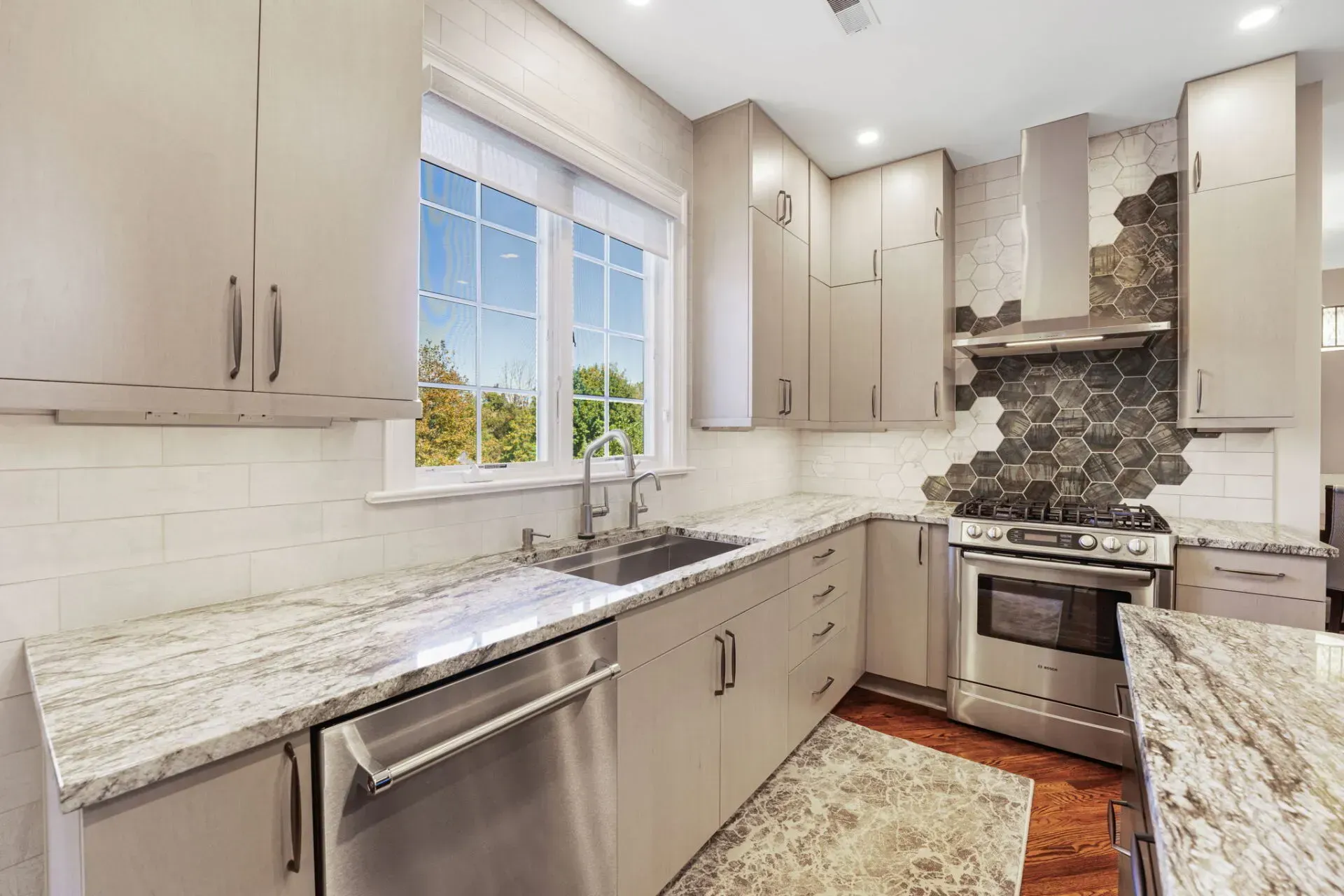 Modern kitchen with light cabinets, marble counters, stainless appliances, and a mosaic tile backsplash In Bucks County PA