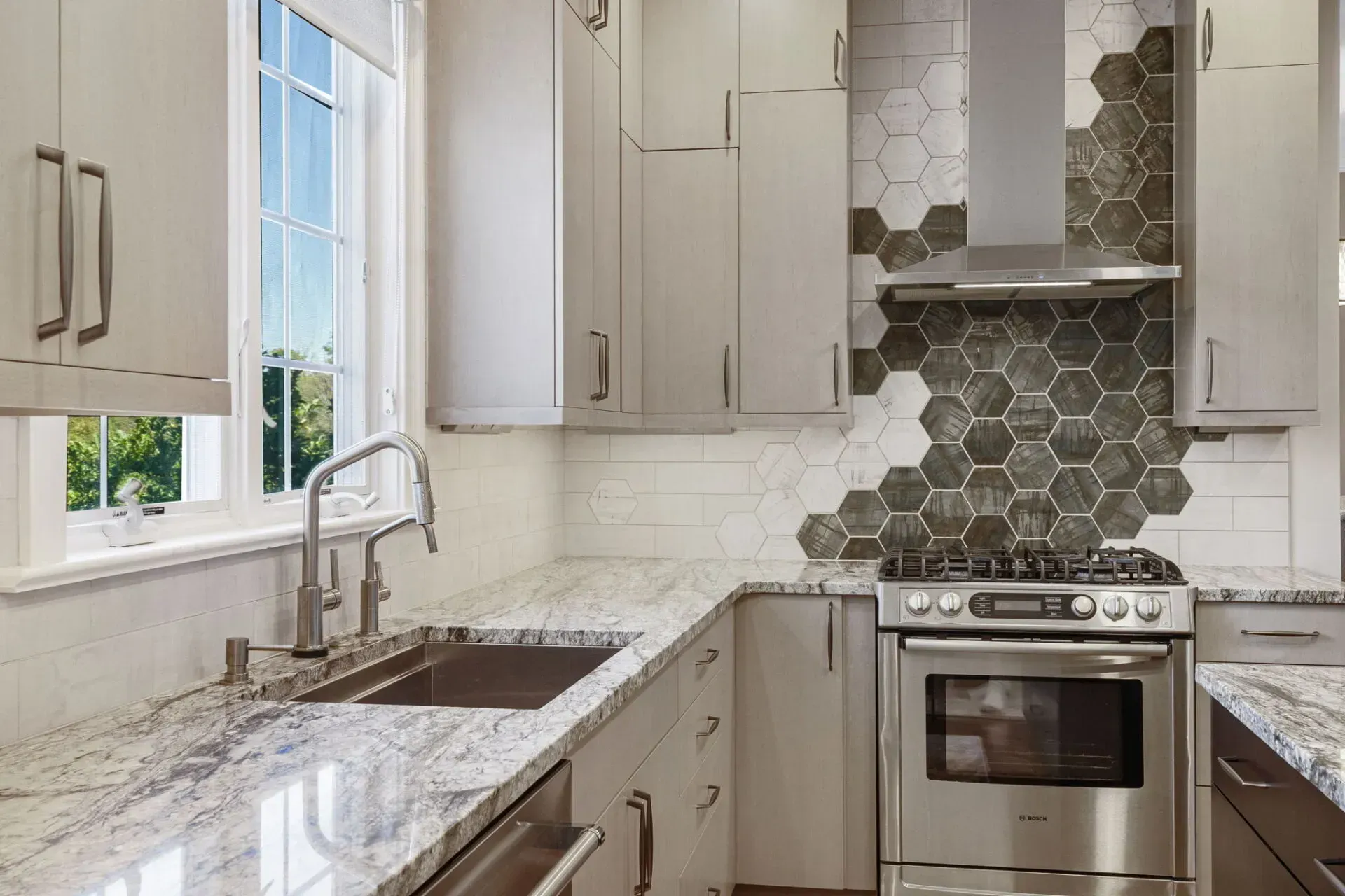 Modern kitchen with white cabinets, marble countertops, stainless stove, and hexagonal tile backsplash In Bucks County PA