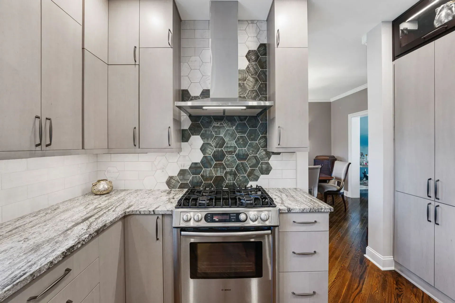 Modern kitchen with light cabinets, granite counters, stainless steel stove, and a gray tile backsplash In Bucks Country PA