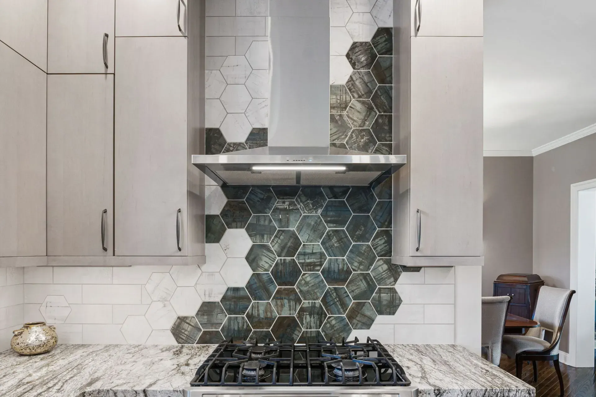 Modern kitchen stove with hexagonal tile backsplash, granite countertop, and light wood cabinets In Bucks County PA