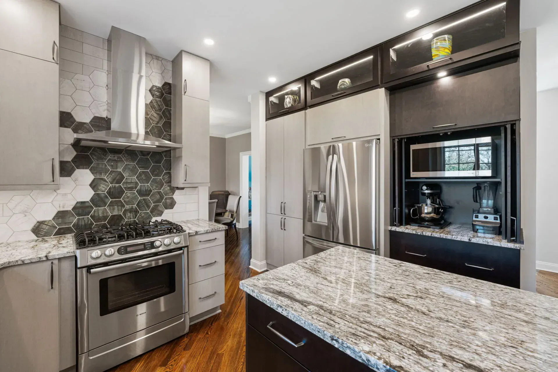Modern kitchen with stainless steel appliances, granite island, and hexagon tile backsplash In Bucks County PA
