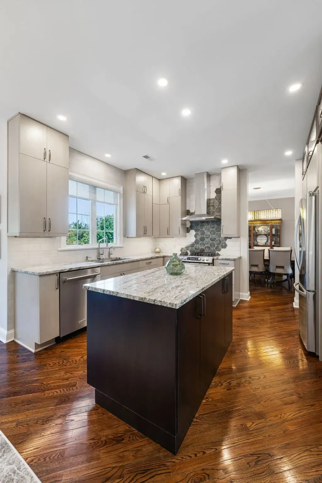 Bright modern kitchen with white cabinets, dark island, granite counters, and hardwood floors In Bucks County PA