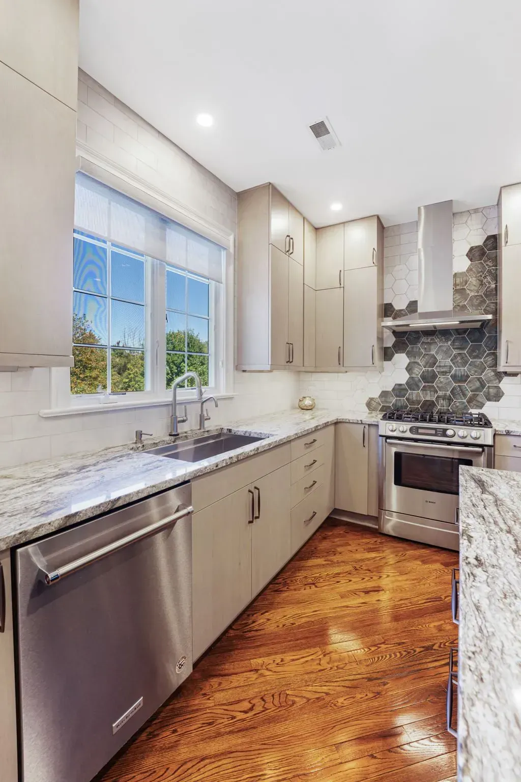 Modern kitchen with stainless steel appliances, white cabinets, granite counters, and a window over the sink In Bucks County PA