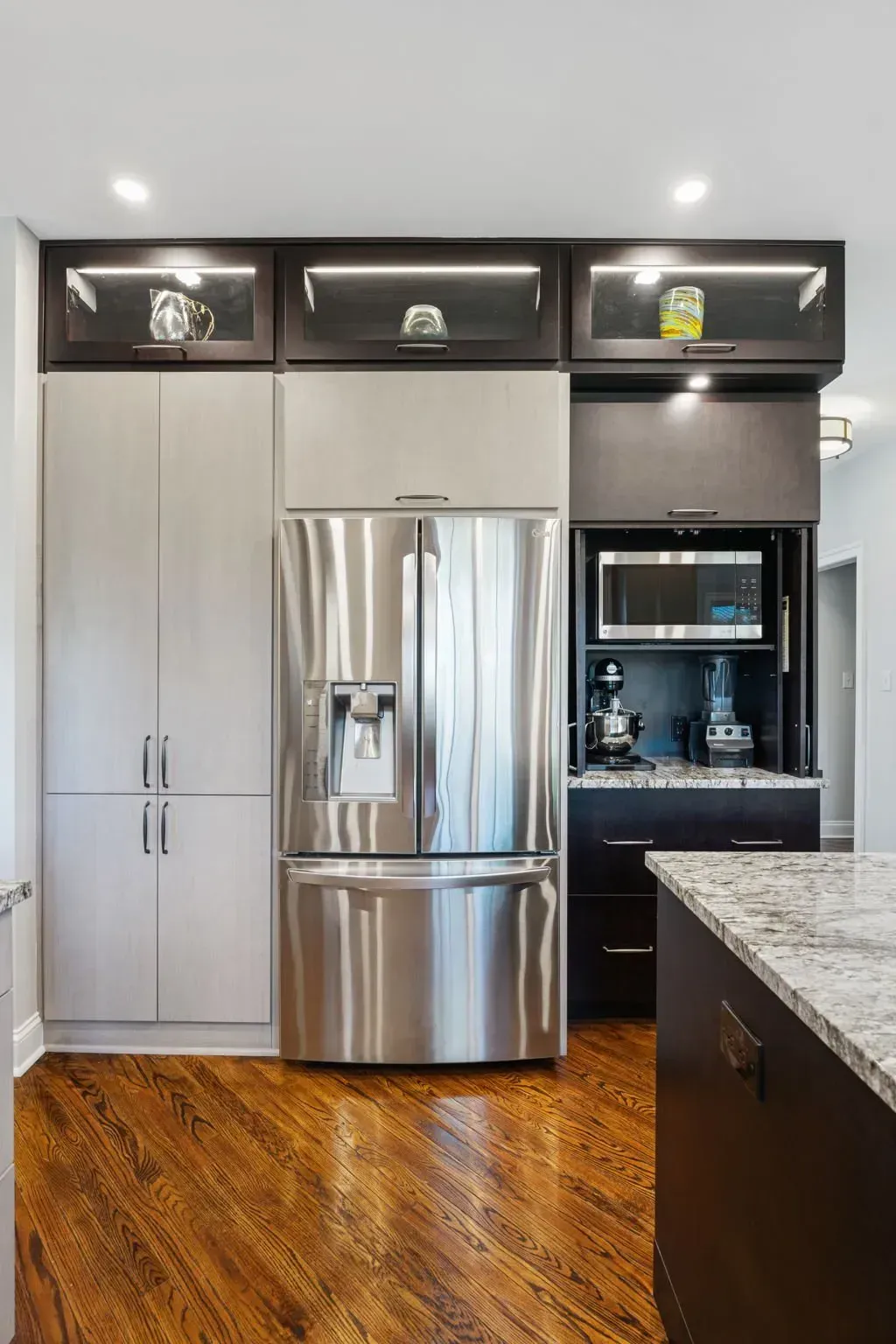 Modern kitchen with stainless steel refrigerator, white cabinets, black shelves, and granite countertop, on wood floor In Bucks County PA