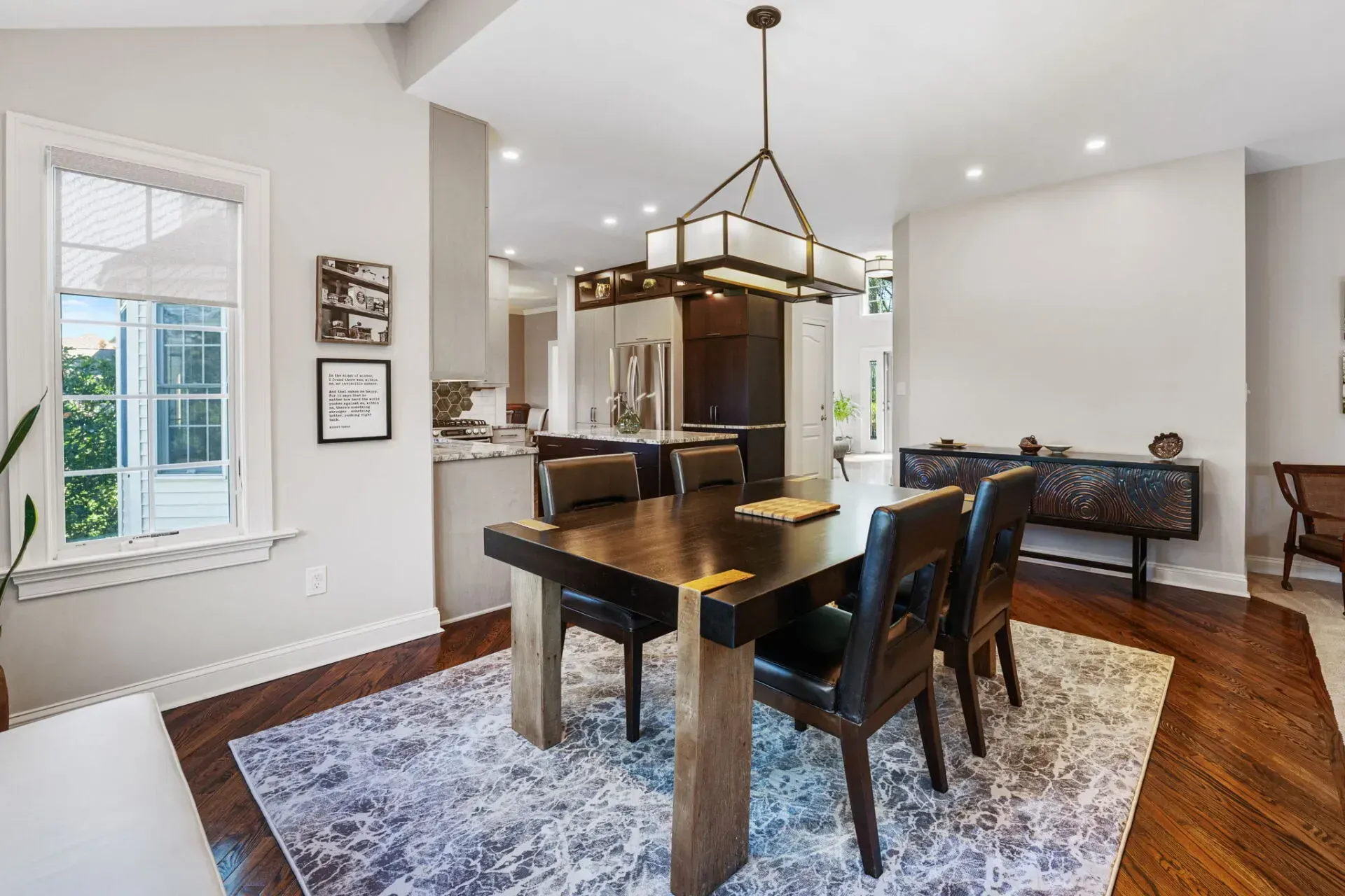 Modern dining room with dark wood table, black chairs, chandelier, and patterned rug under bright windows In Bucks County PA