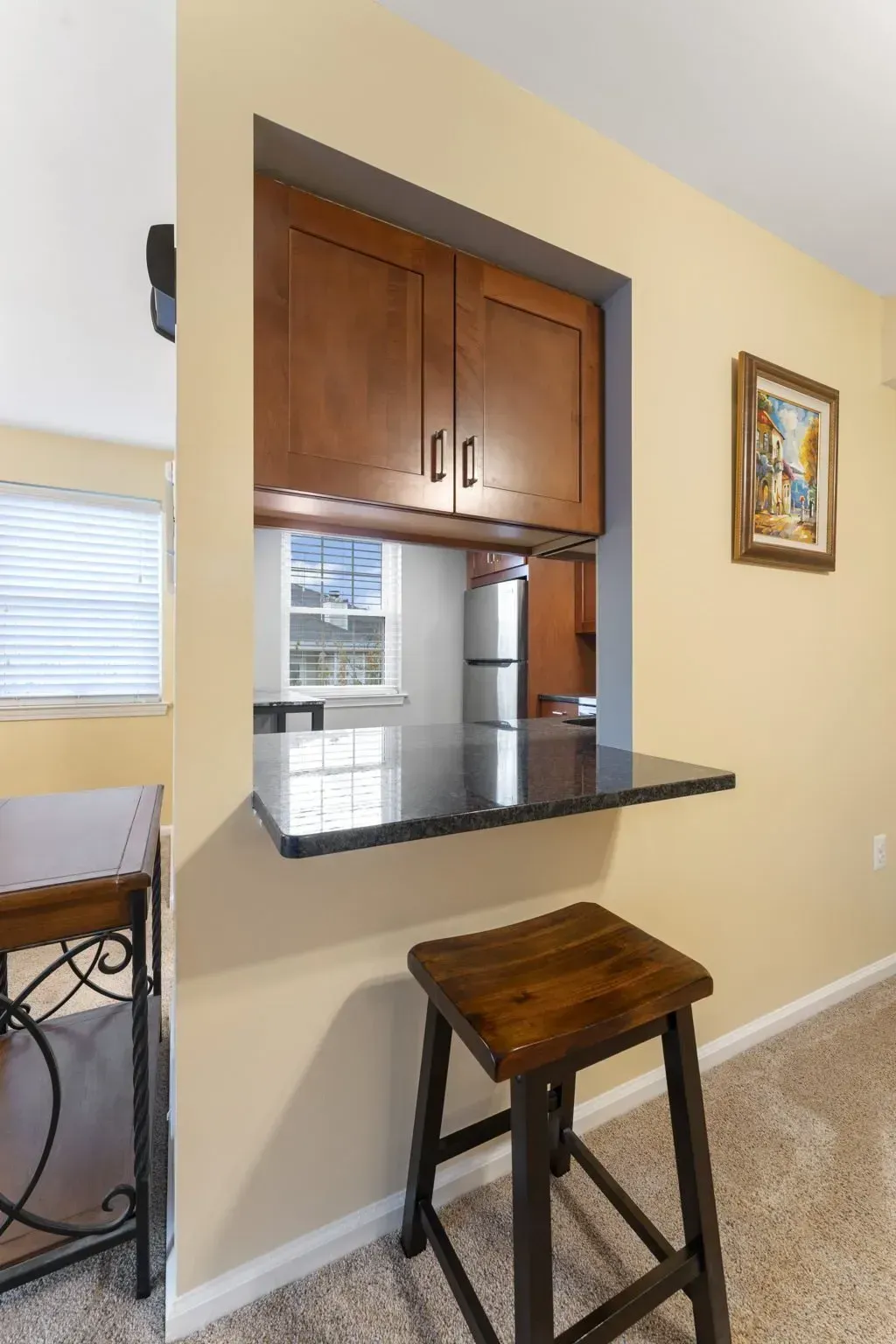 Kitchen pass-through with wood cabinets, black countertop, stool, and framed wall art on beige wall In Bucks County PA