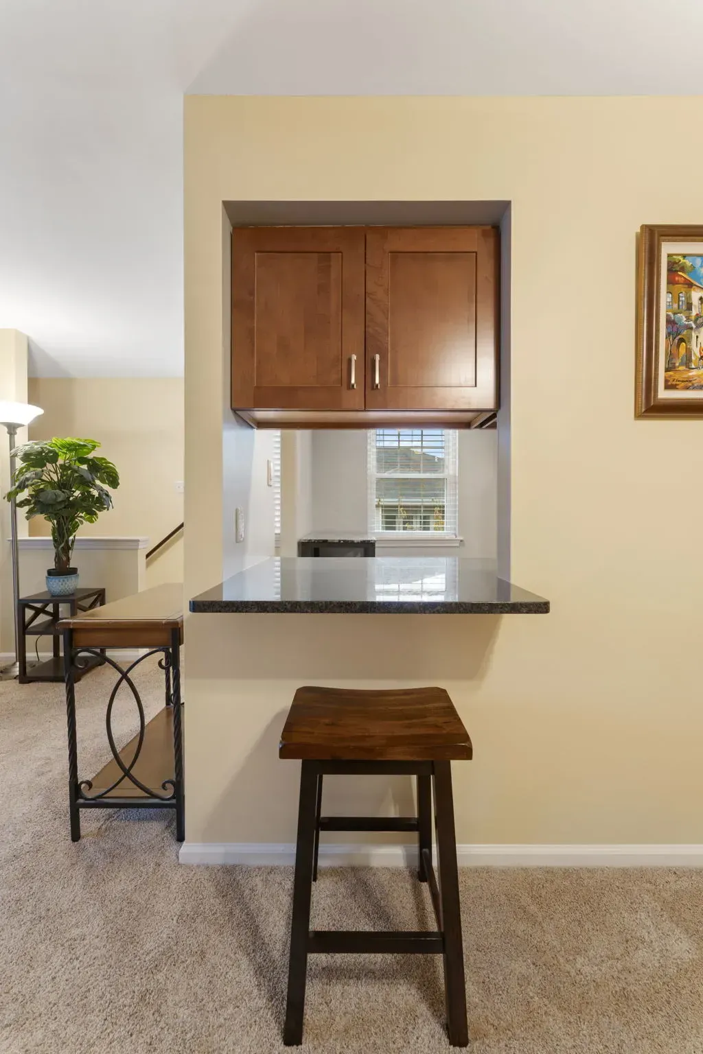 Small kitchen pass-through with a dark countertop, wood cabinet, and a stool in front In Bucks County PA