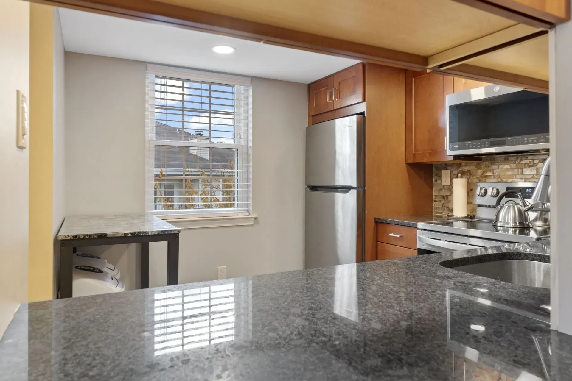 Modern kitchen with granite countertop, wooden cabinets, stainless steel appliances, and a window In Bucks County PA