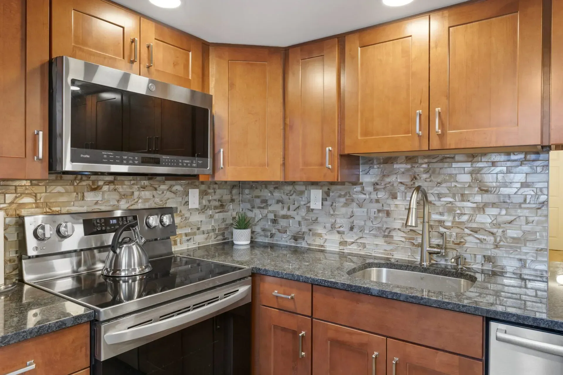 Modern kitchen with wood cabinets, stainless steel appliances, granite counters, and stone tile backsplash In Bucks County PA