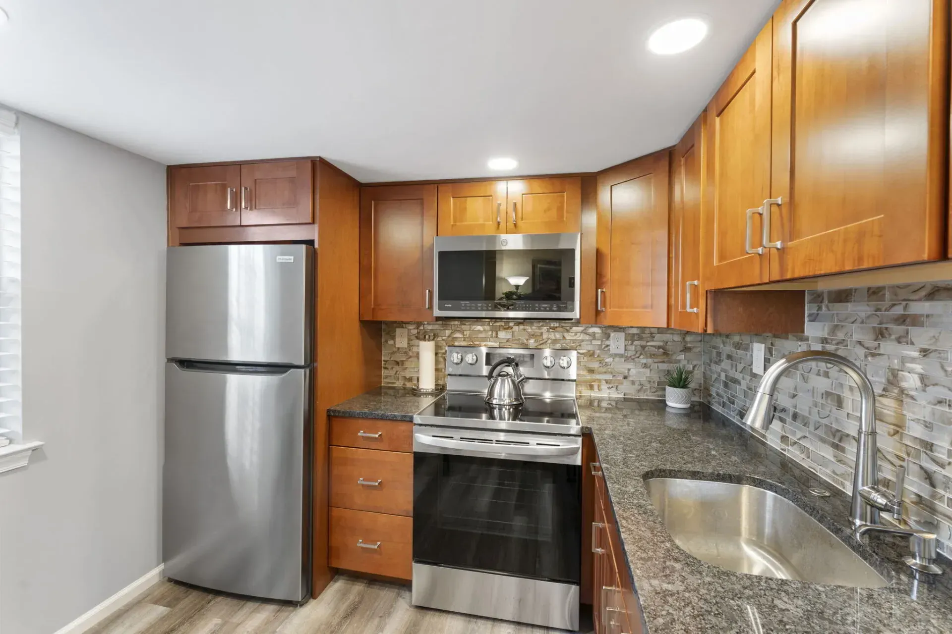 Modern kitchen with stainless steel appliances, wood cabinets, granite counters, and a tiled backsplash In Bucks County PA