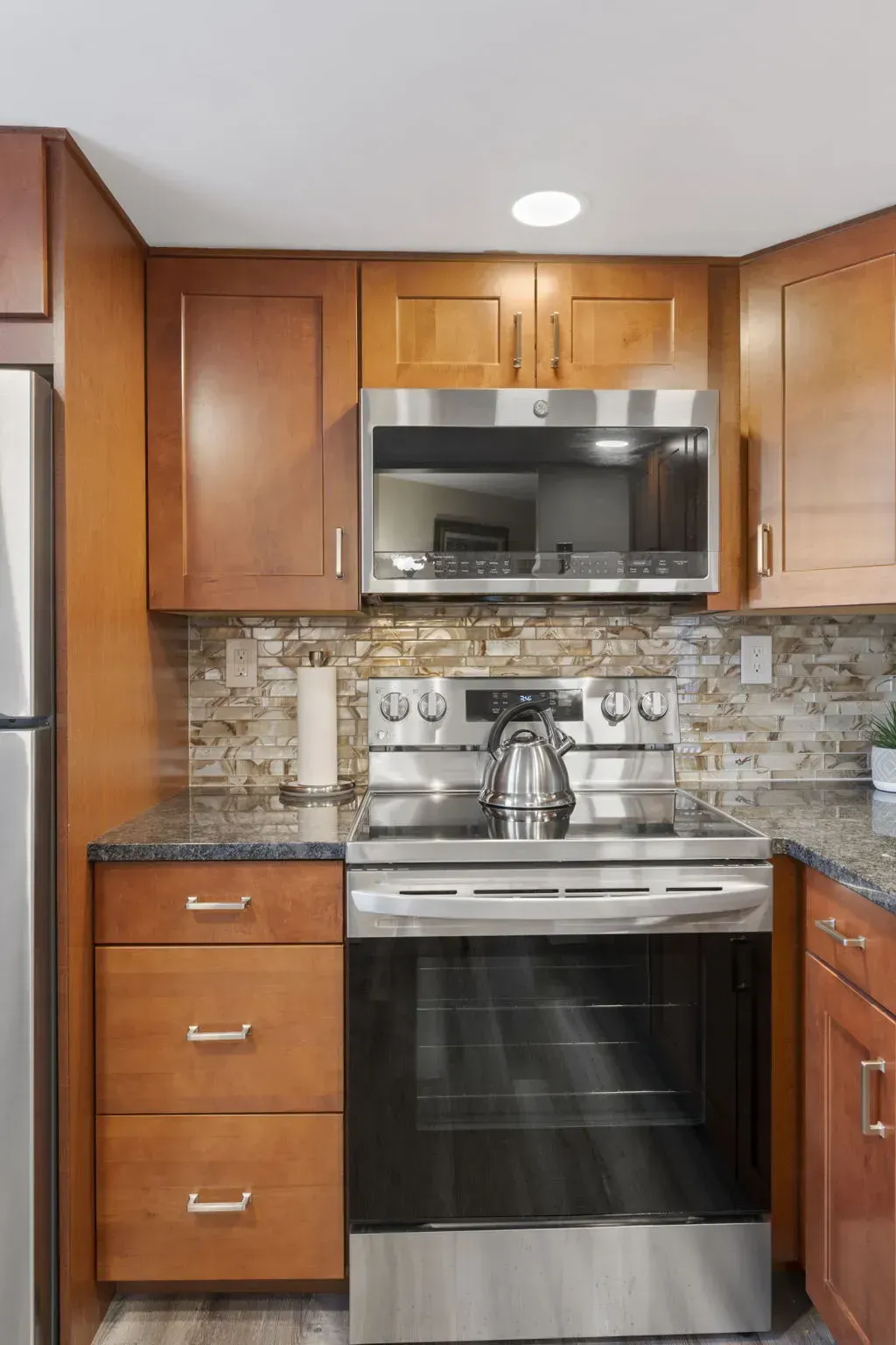 Compact kitchen with wood cabinets, stainless steel stove and microwave, mosaic tile backsplash, and granite countertops In Bucks County PA