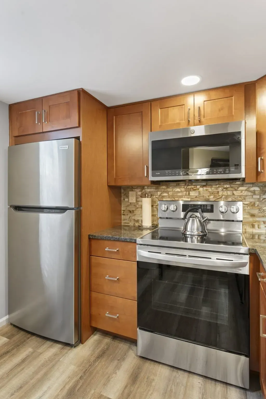 Compact kitchen with stainless steel fridge, stove, and microwave, wood cabinets, and tiled backsplash In Bucks County PA