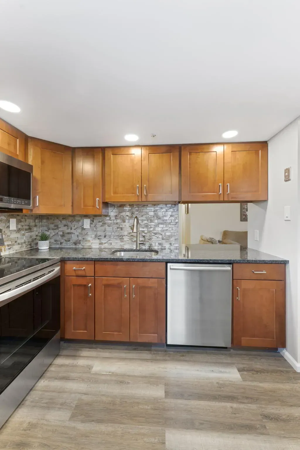 Small kitchen with wood cabinets, stainless dishwasher, mosaic backsplash, and light gray flooring In Bucks County PA