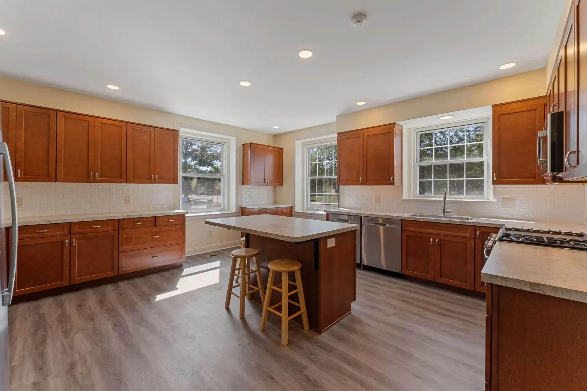 Spacious kitchen with wood cabinets, gray floors, island seating, and large windows  In Bucks County PA