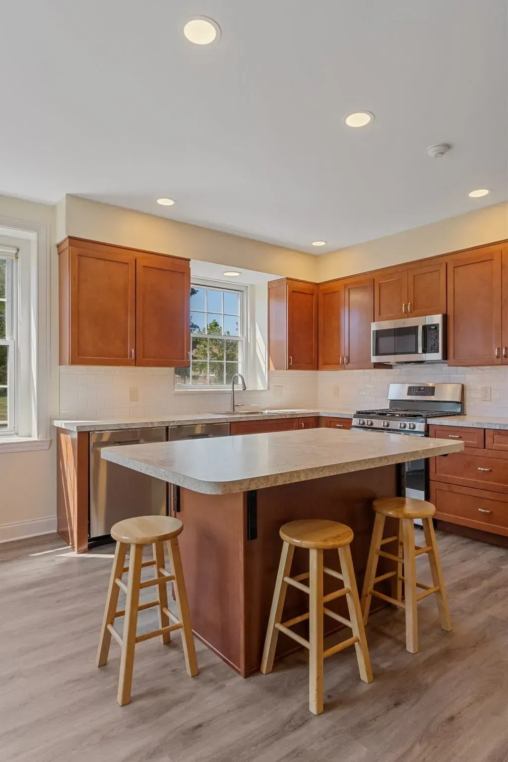 Bright kitchen with wooden cabinets, white island, and three stools under recessed lights  In Bucks County PA