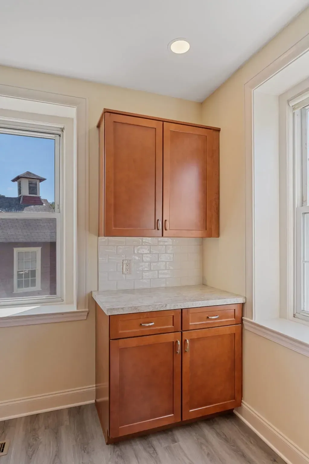 Built-in wooden cabinets in a small alcove between two windows, with white tile backsplash  In Bucks County PA