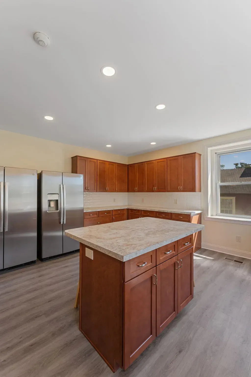 Empty modern kitchen with stainless steel refrigerator, wood cabinets, and a central island with granite countertop  In Bucks County PA