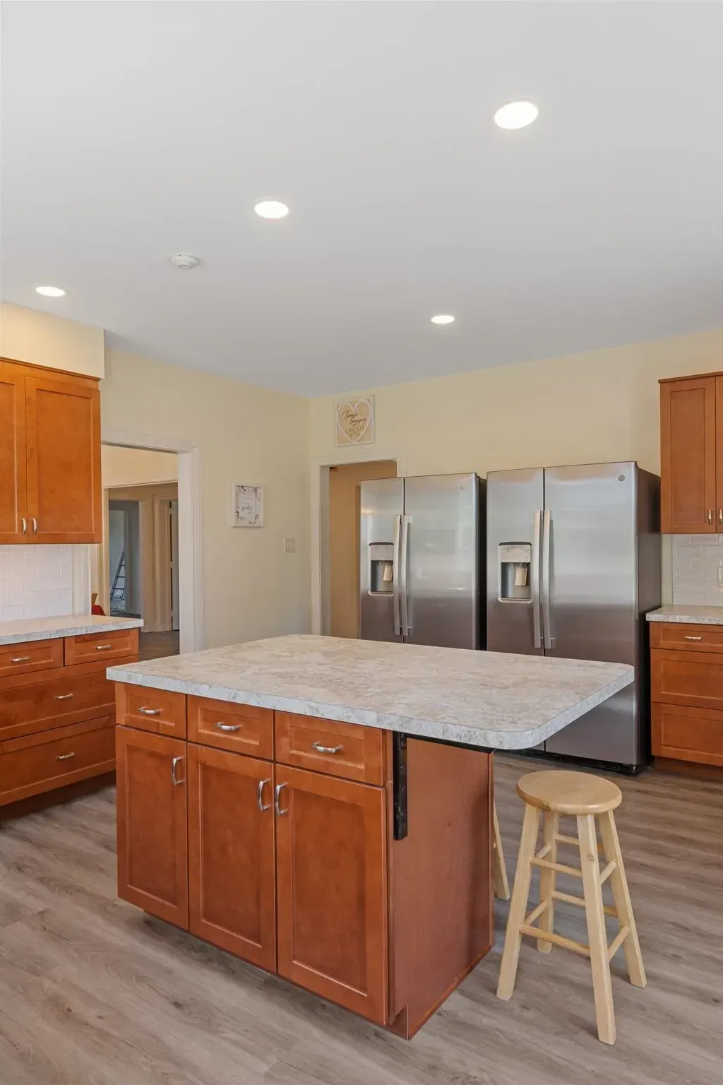 Bright kitchen with wood cabinets, large island, stainless steel fridge, and stool on light wood floor  In Bucks County PA