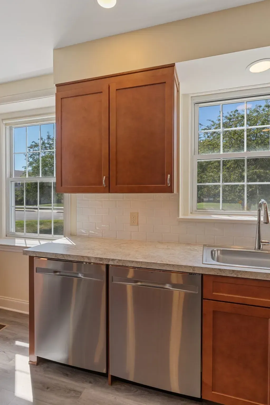 Modern kitchen with stainless steel dishwasher, wood cabinets, and two windows above the counter  In Bucks County PA