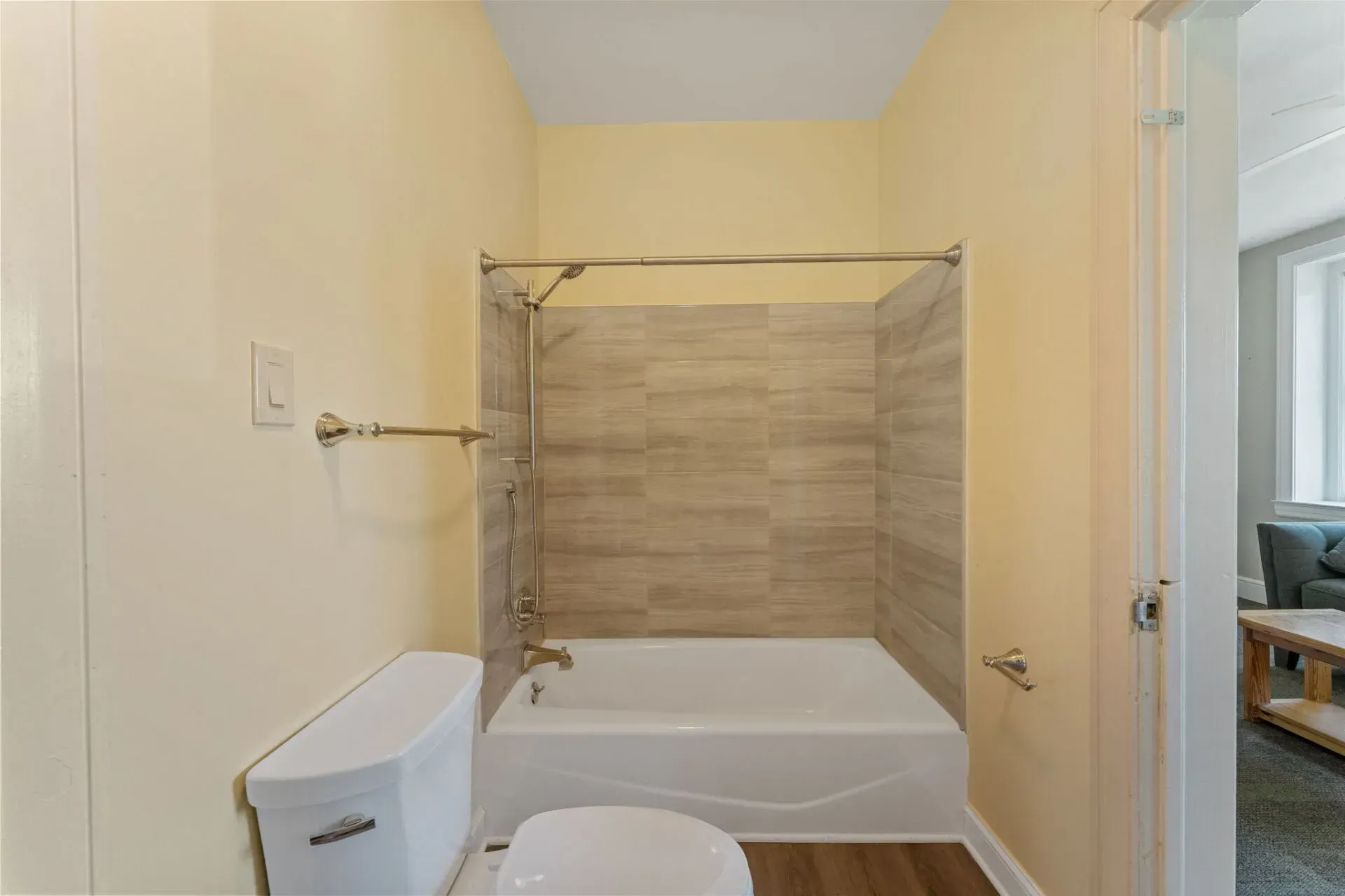Bathroom with a white tub, tan tile shower surround, and a toilet in the foreground  In Bucks County PA