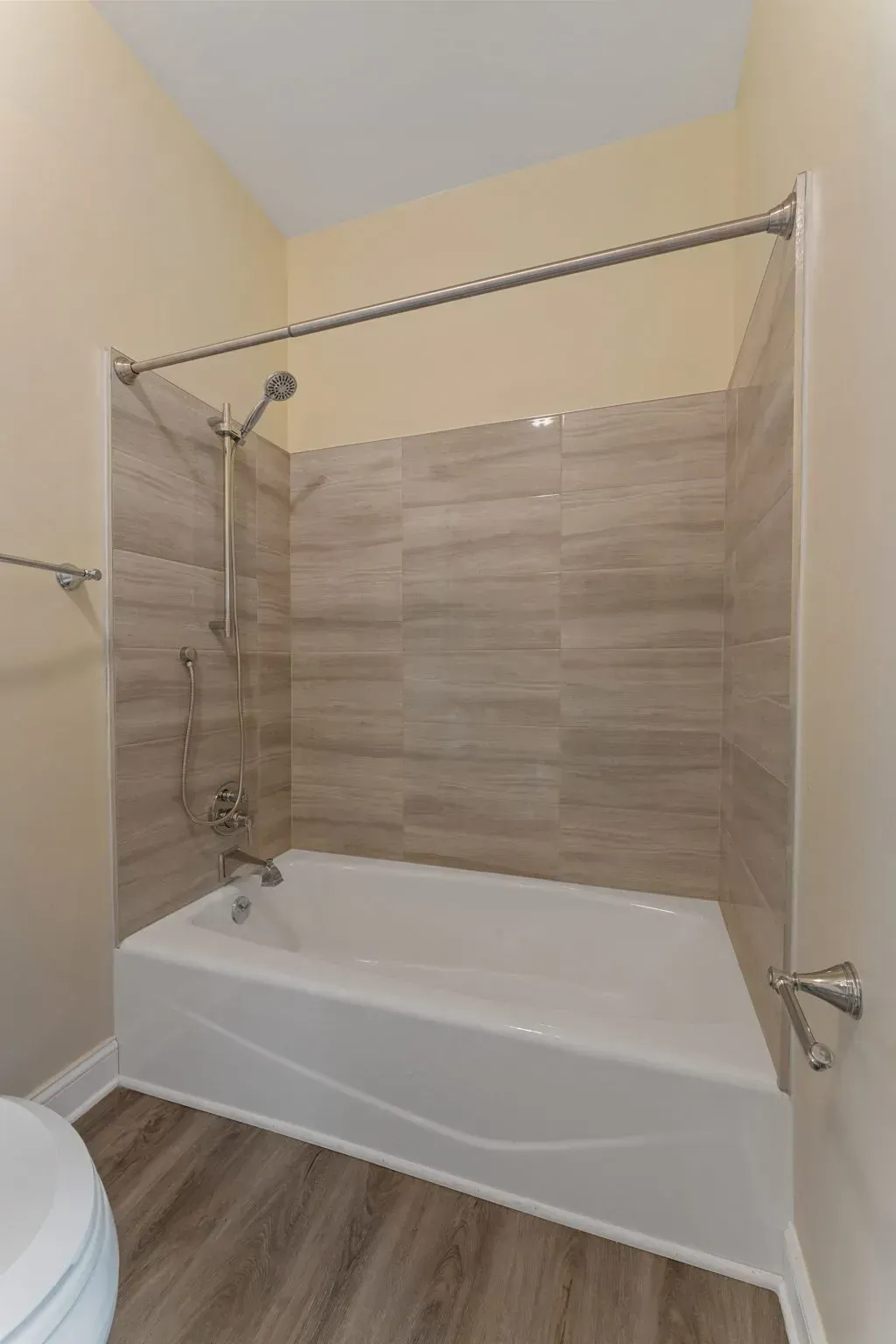 Bathroom with a white tub, beige tile surround, and curved shower curtain rod under a sloped ceiling  In Bucks County PA
