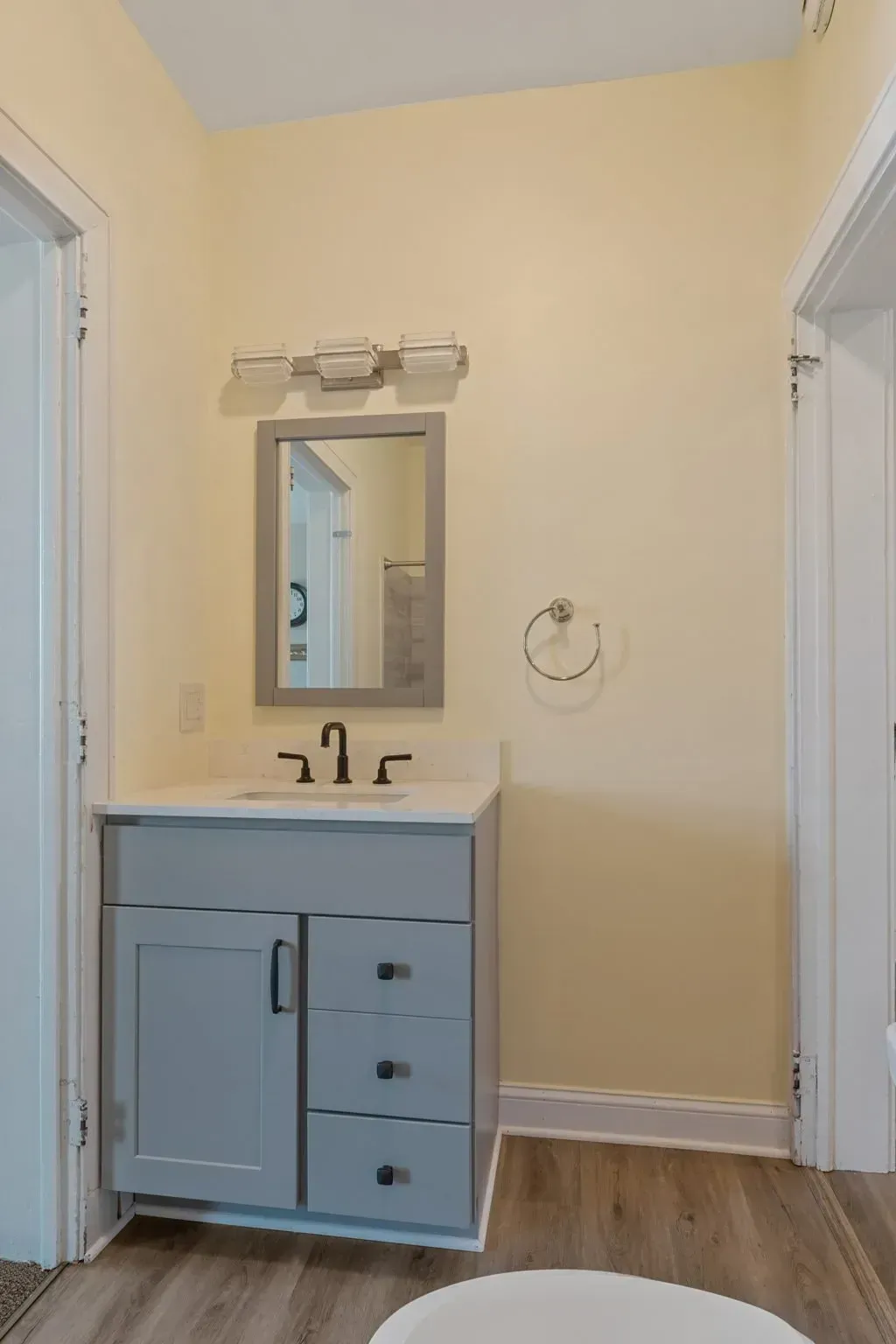 Small bathroom vanity with mirror, light blue cabinet, and towel ring on a cream wall  In Bucks County PA