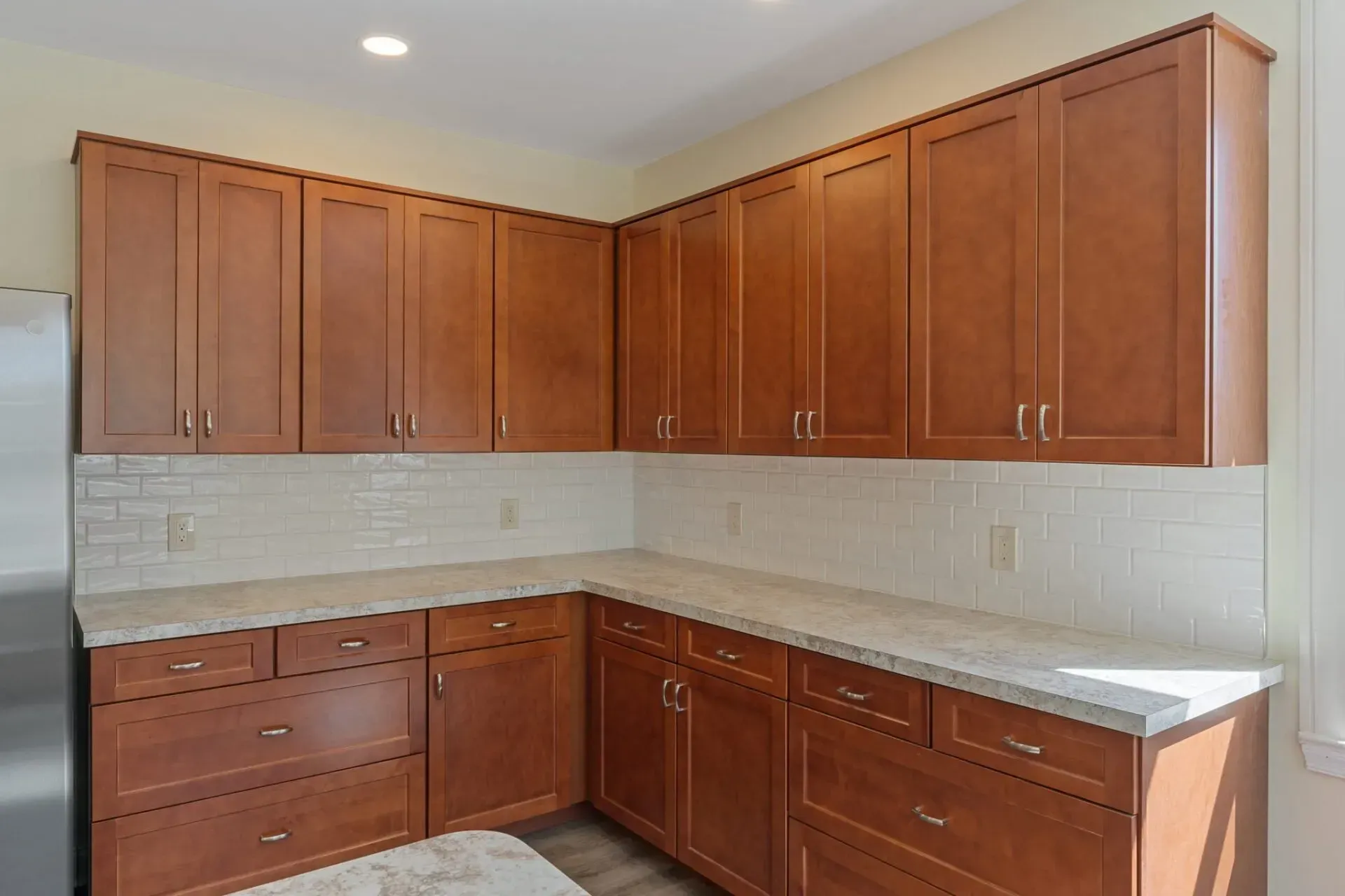 Empty kitchen with brown wood cabinets, light countertops, and white tile backsplash  In Bucks County PA
