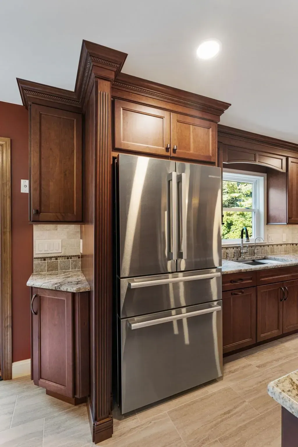 Kitchen with stainless steel refrigerator, dark wood cabinets, and granite countertops in warm lighting  In Bucks County PA