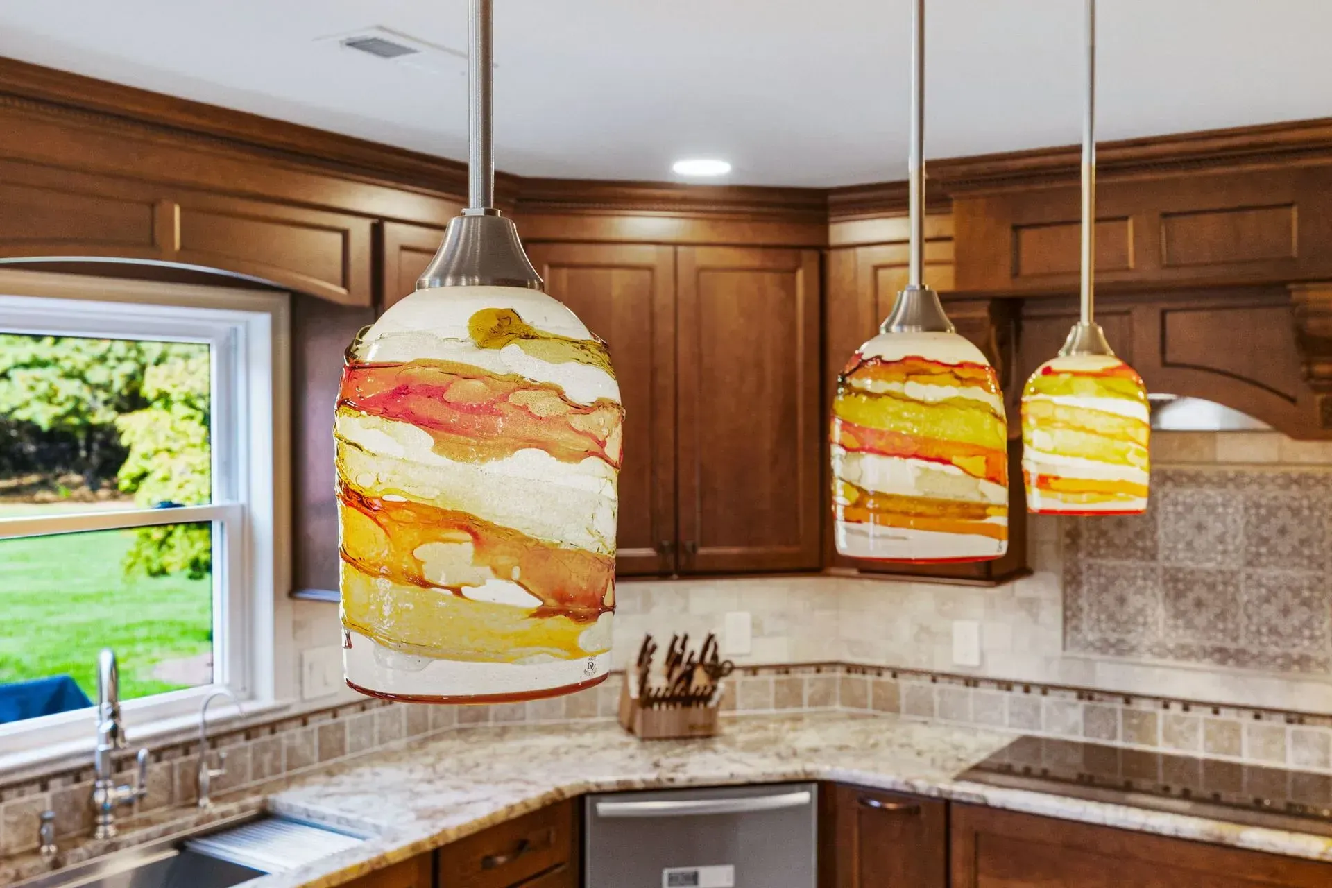 Kitchen with three colorful pendant lights hanging over a granite countertop and wood cabinets.