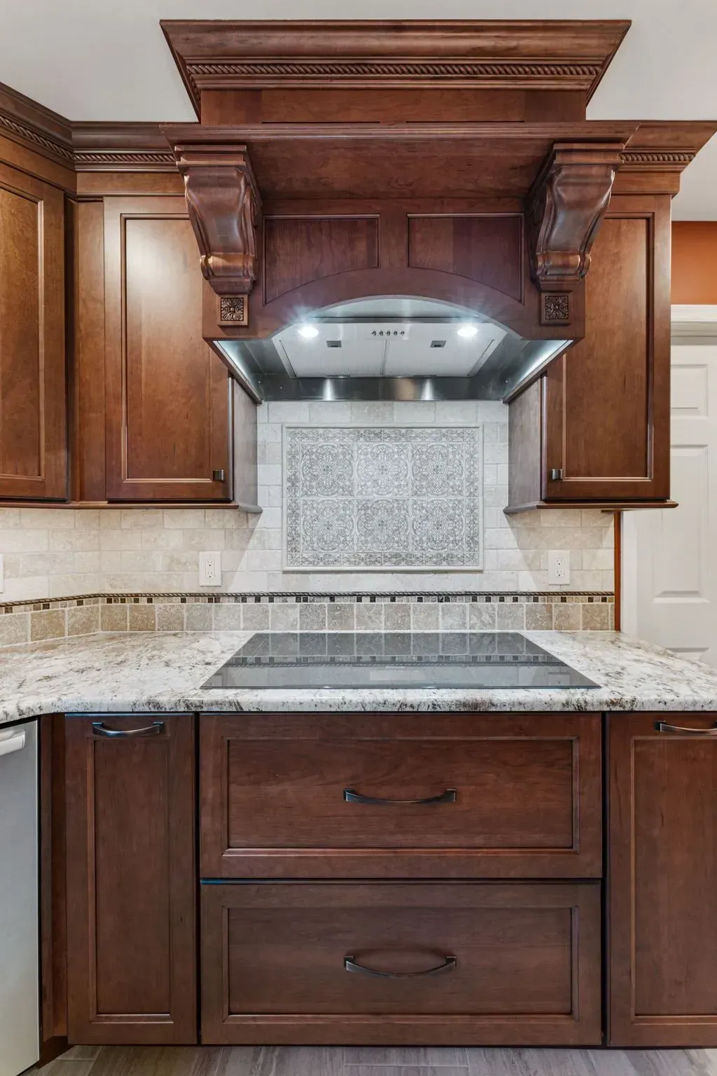 Dark wood kitchen cabinets with ornate range hood, granite countertop, and tiled backsplash  In Bucks County PA
