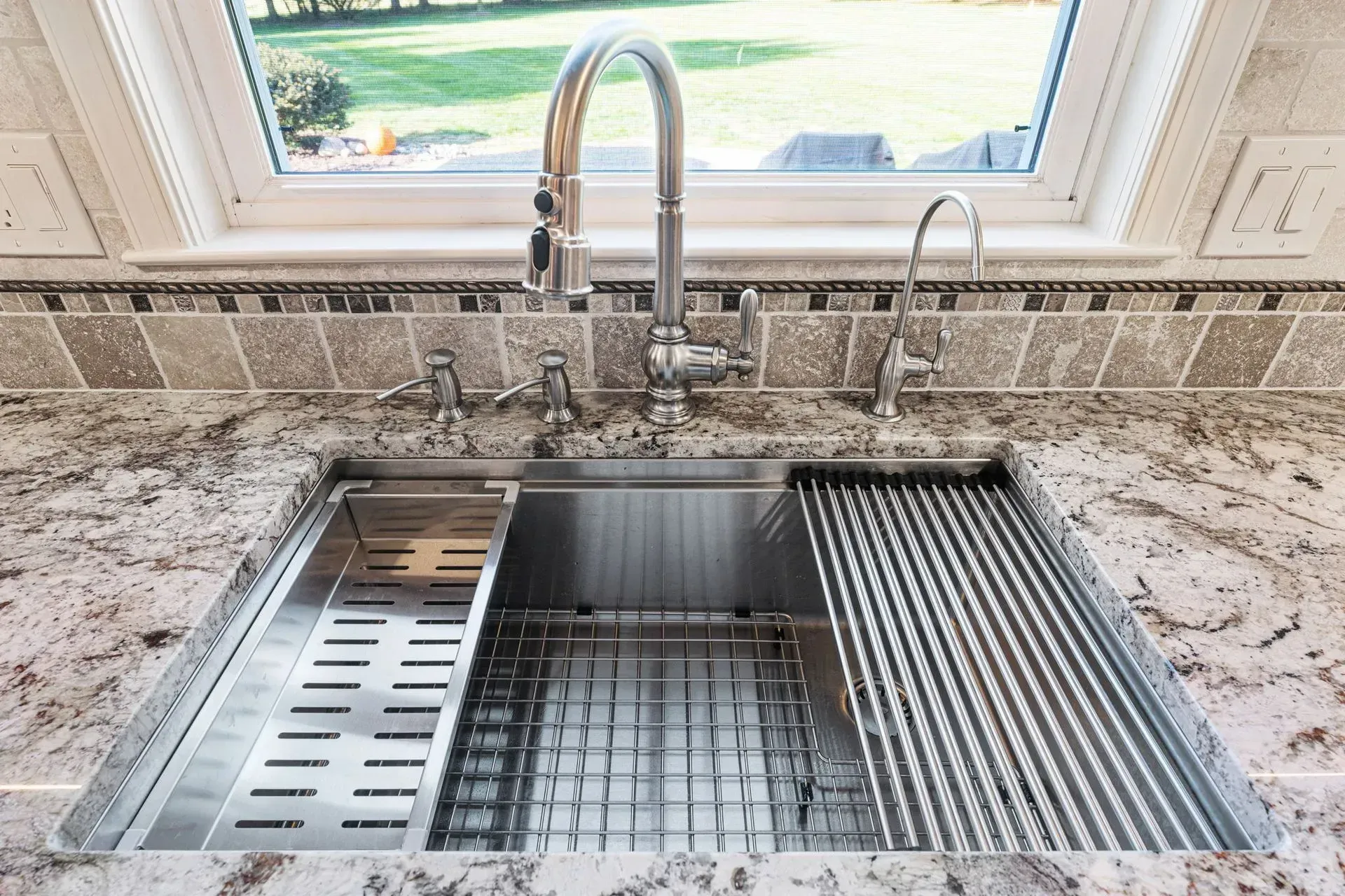 Kitchen sink with stainless-steel basin, gooseneck faucet, and speckled countertop beneath a window  In Bucks County PA